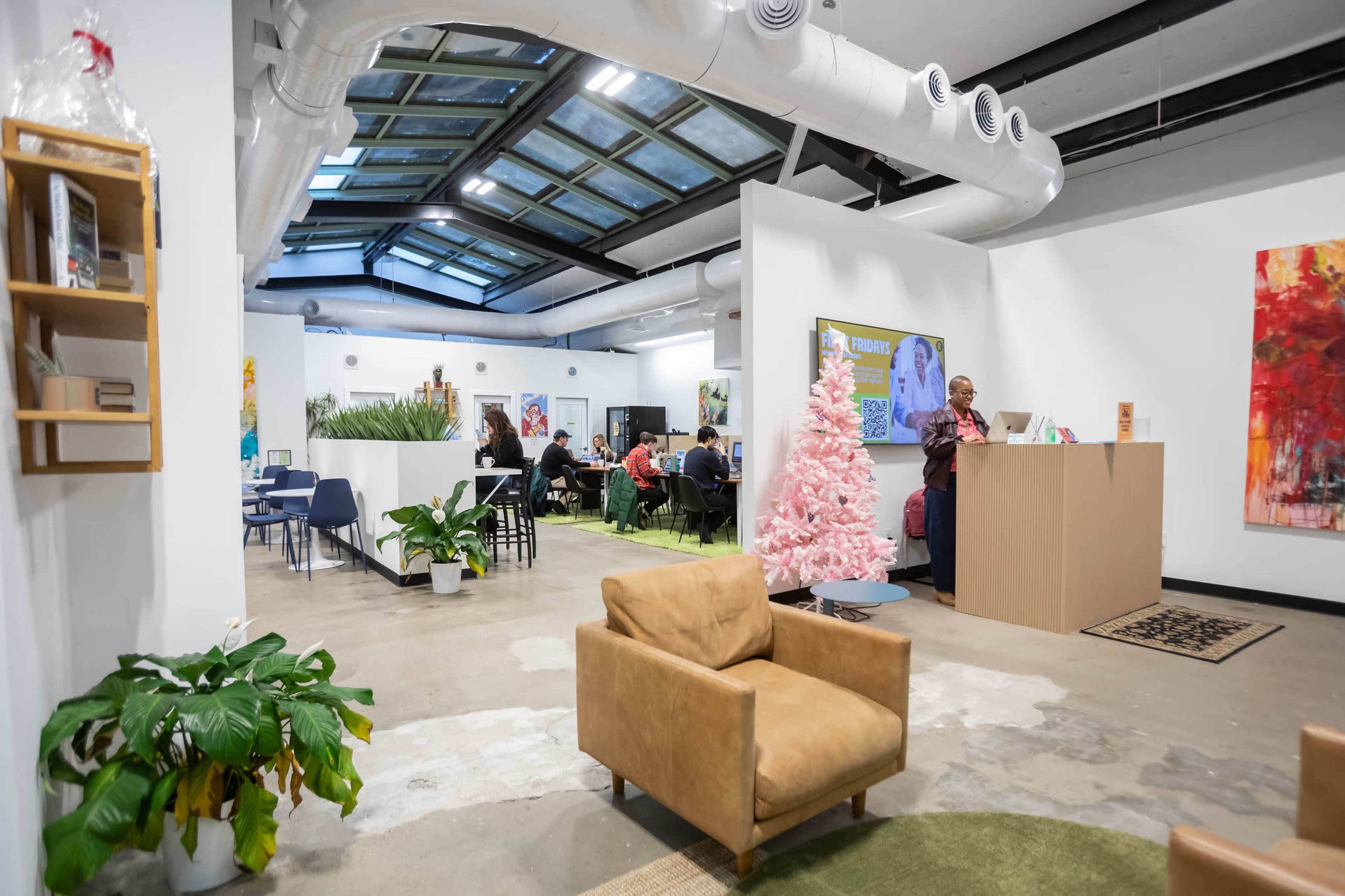 The image shows a modern, open workspace with a seating area, a reception desk, and several people engaged in conversation and work.
