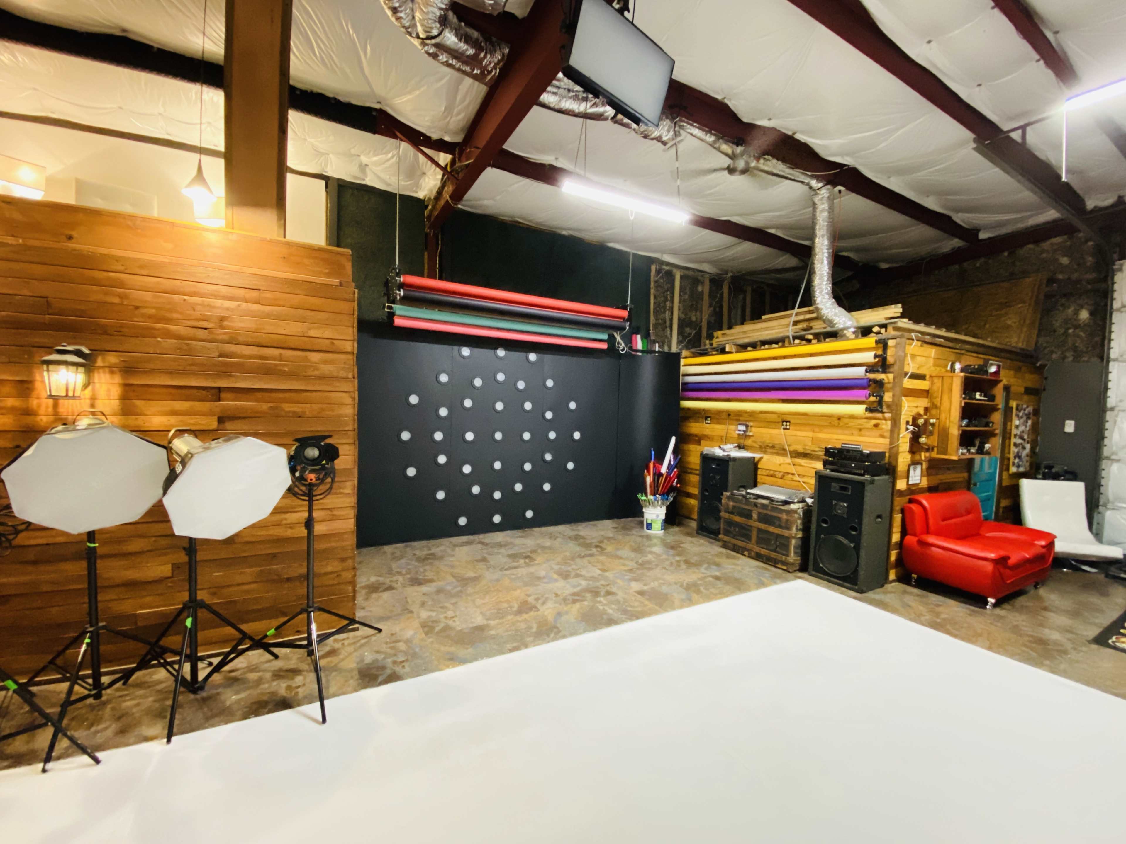 A photography studio with a white backdrop, lighting equipment, colored backdrops on the wall, and wooden accents.