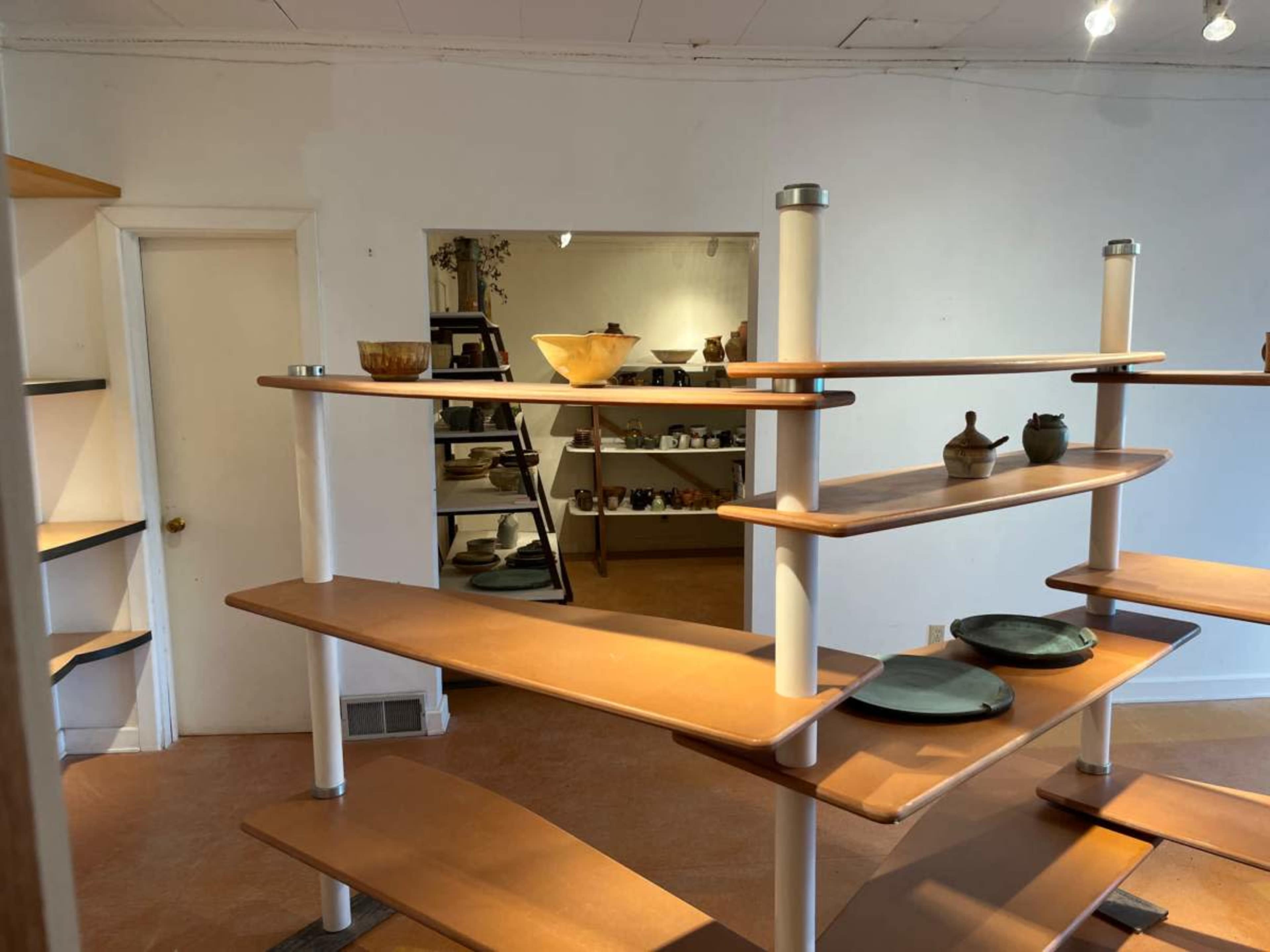 A modern display shelving unit showcases various pottery and dishes in a well-lit room.