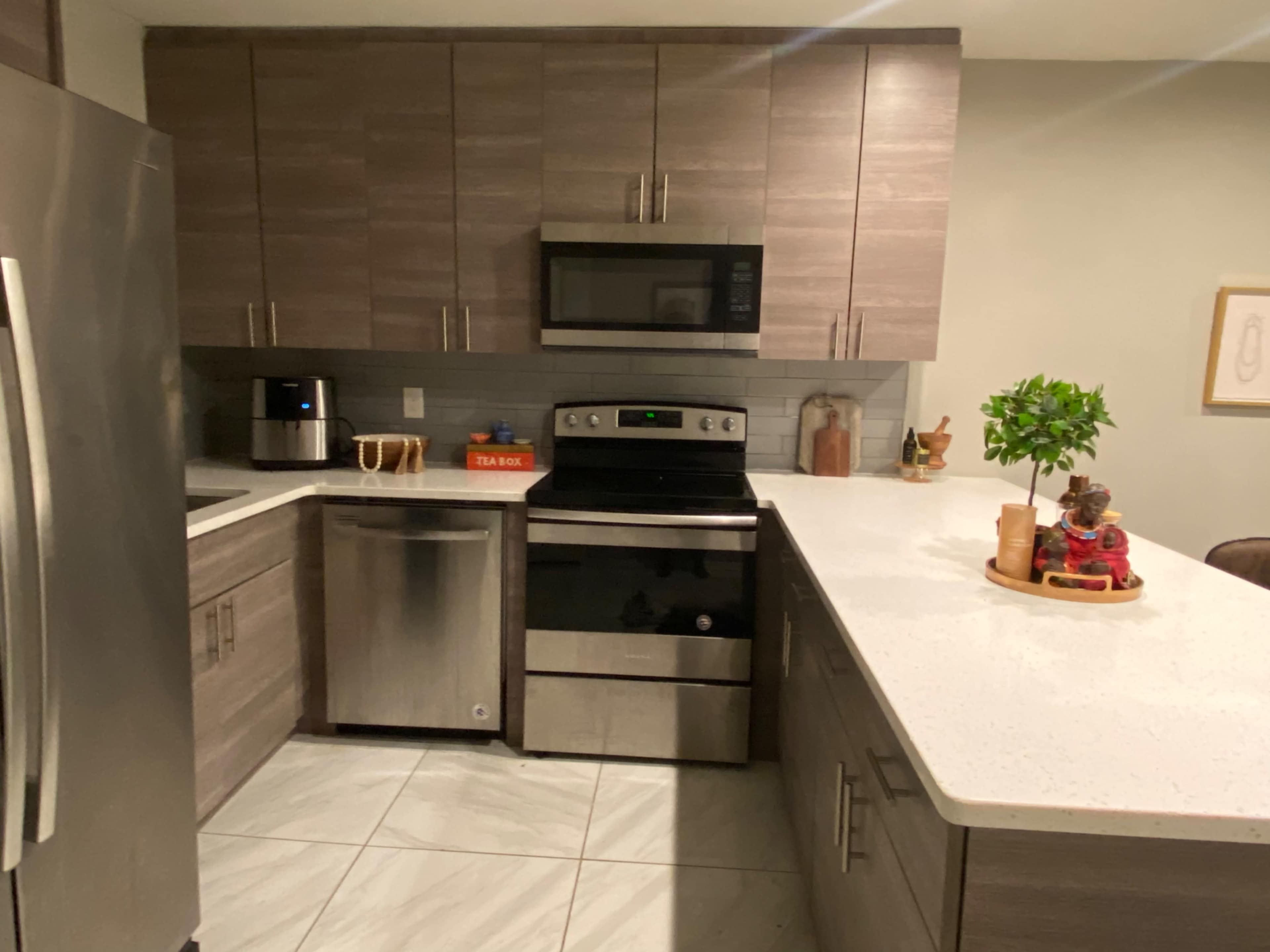 A modern kitchen with stainless steel appliances, gray cabinets, and a white countertop.