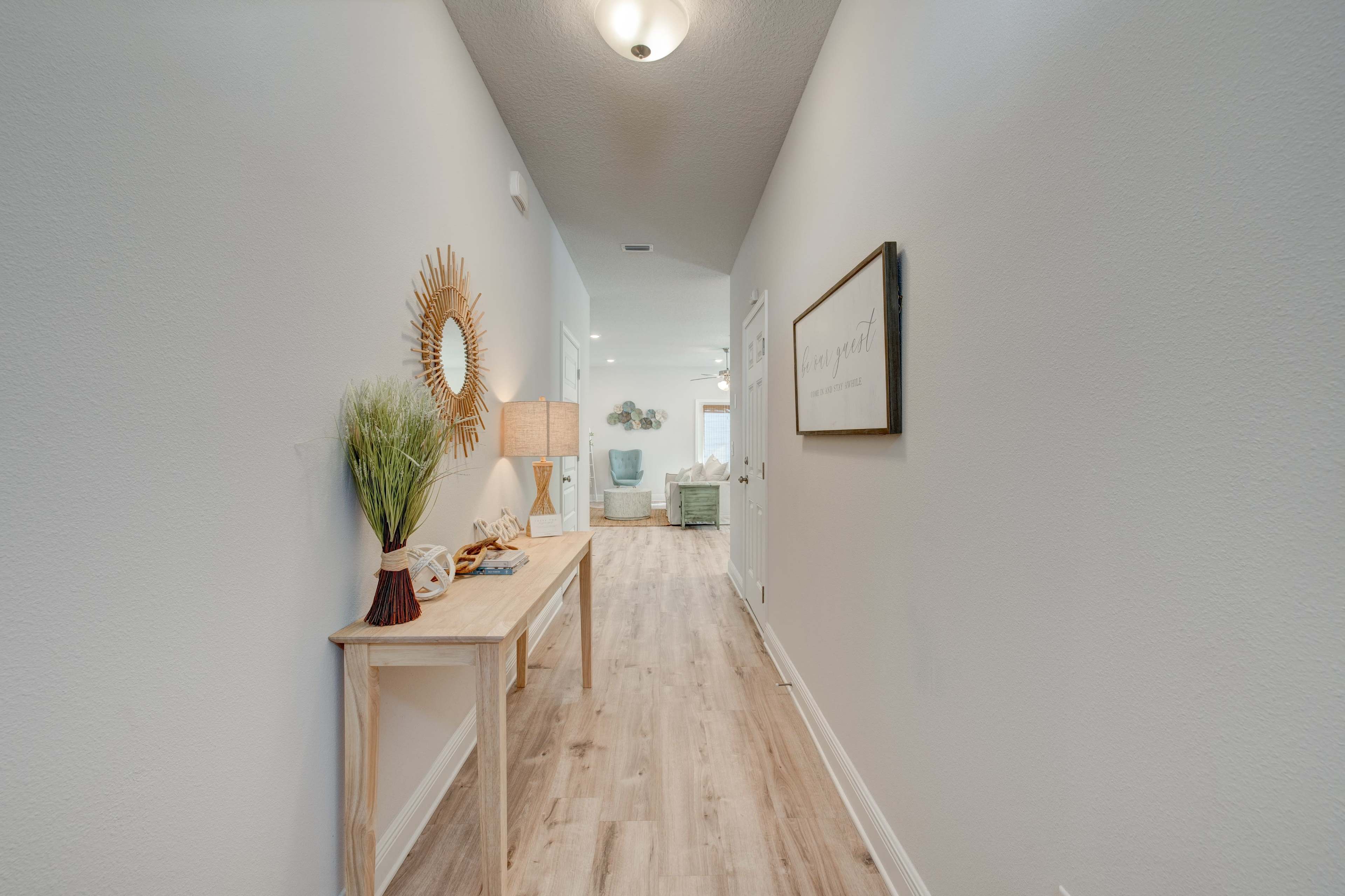 A hallway features a wooden console table with decorative items and a large mirror, leading to a brightly lit living space at the end.