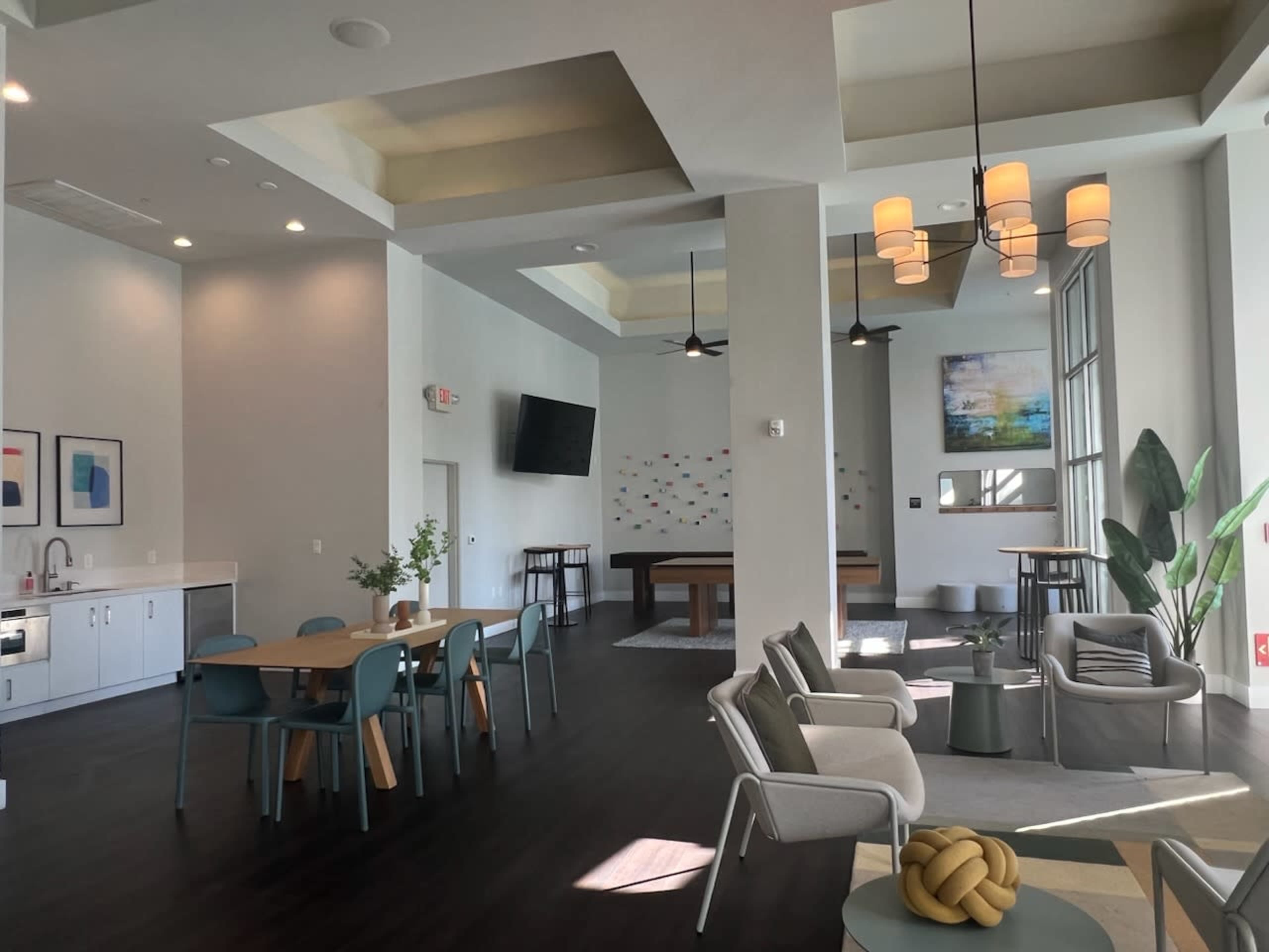 The image shows a modern lounge area featuring a seating arrangement with chairs and a table, a pool table, and large windows allowing natural light to enter.