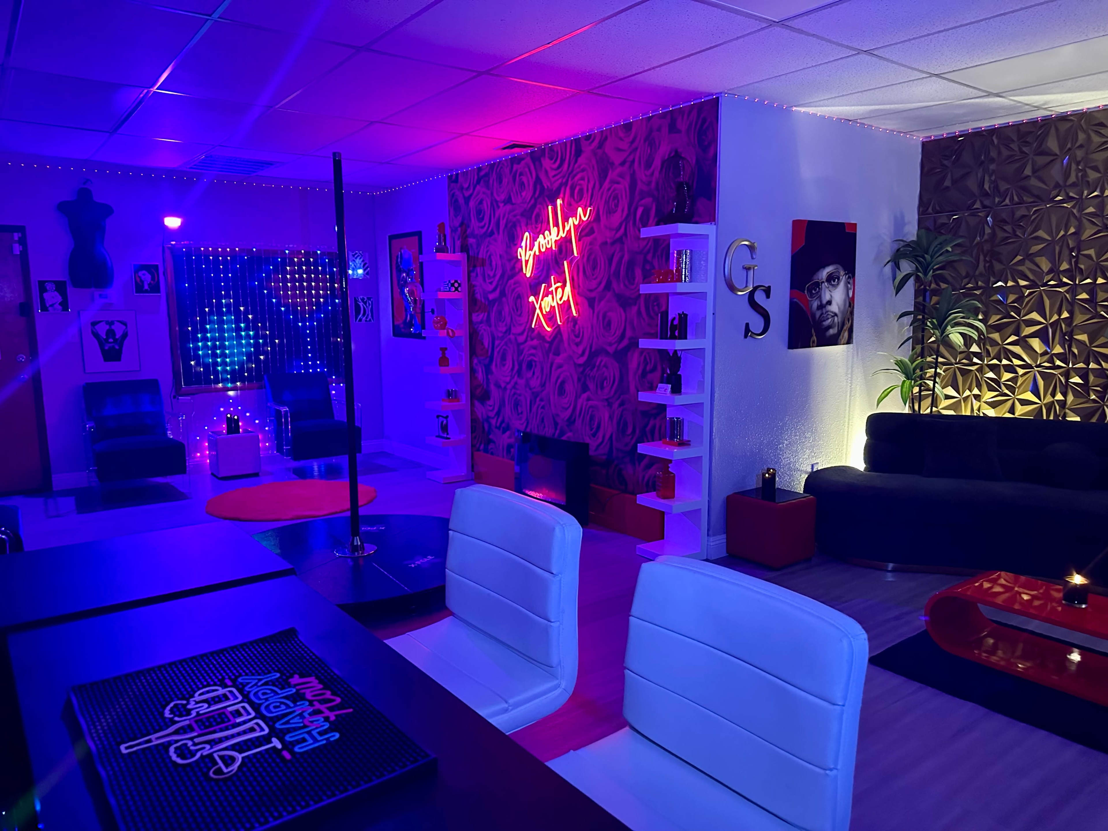 A vibrant lounge area with colorful lighting, modern furniture, and wall art, including a pole and decorative shelves.