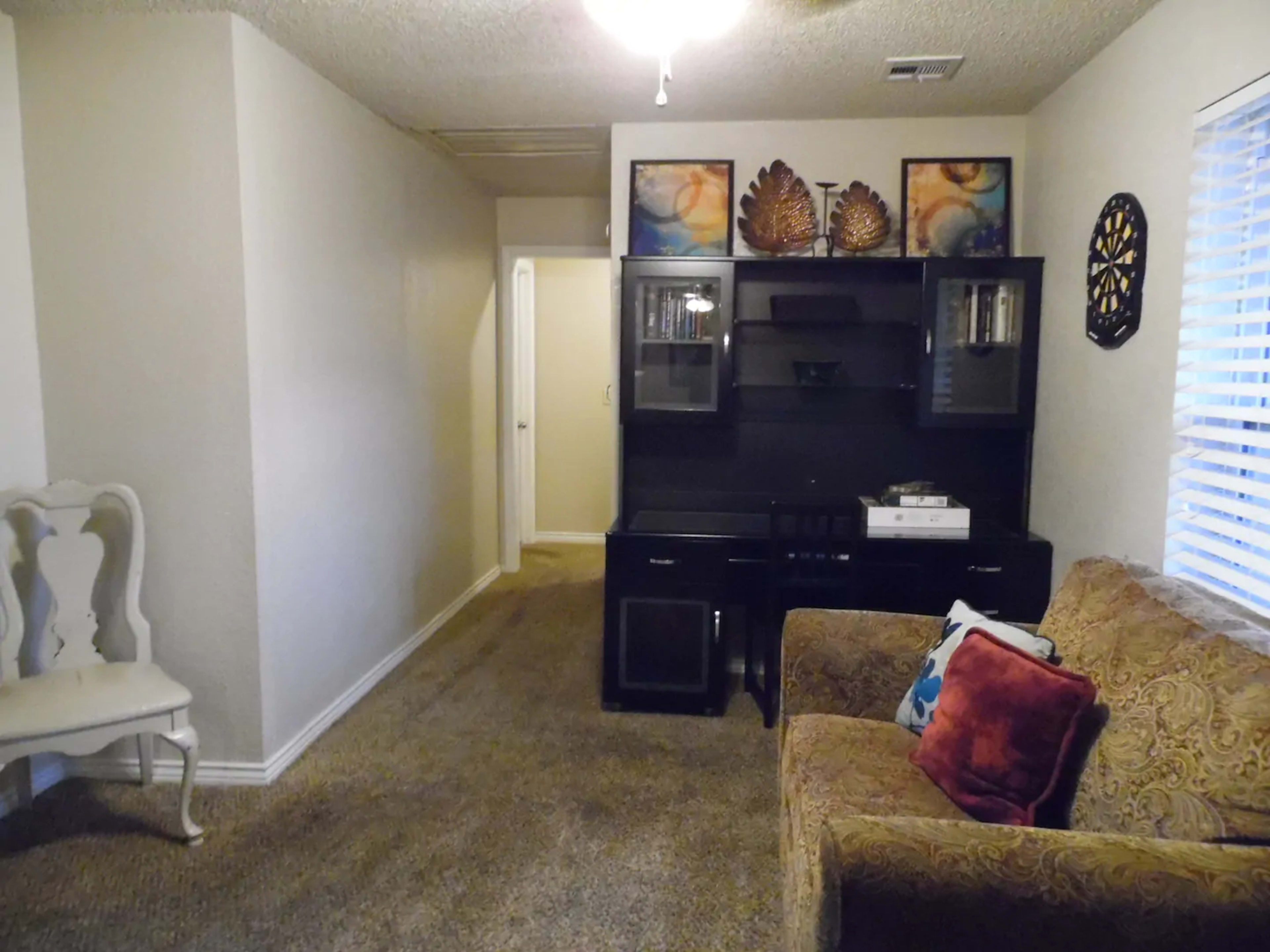 A small living area featuring a couch with patterned cushions, a black shelving unit with decorative items, and a hallway leading to another room.