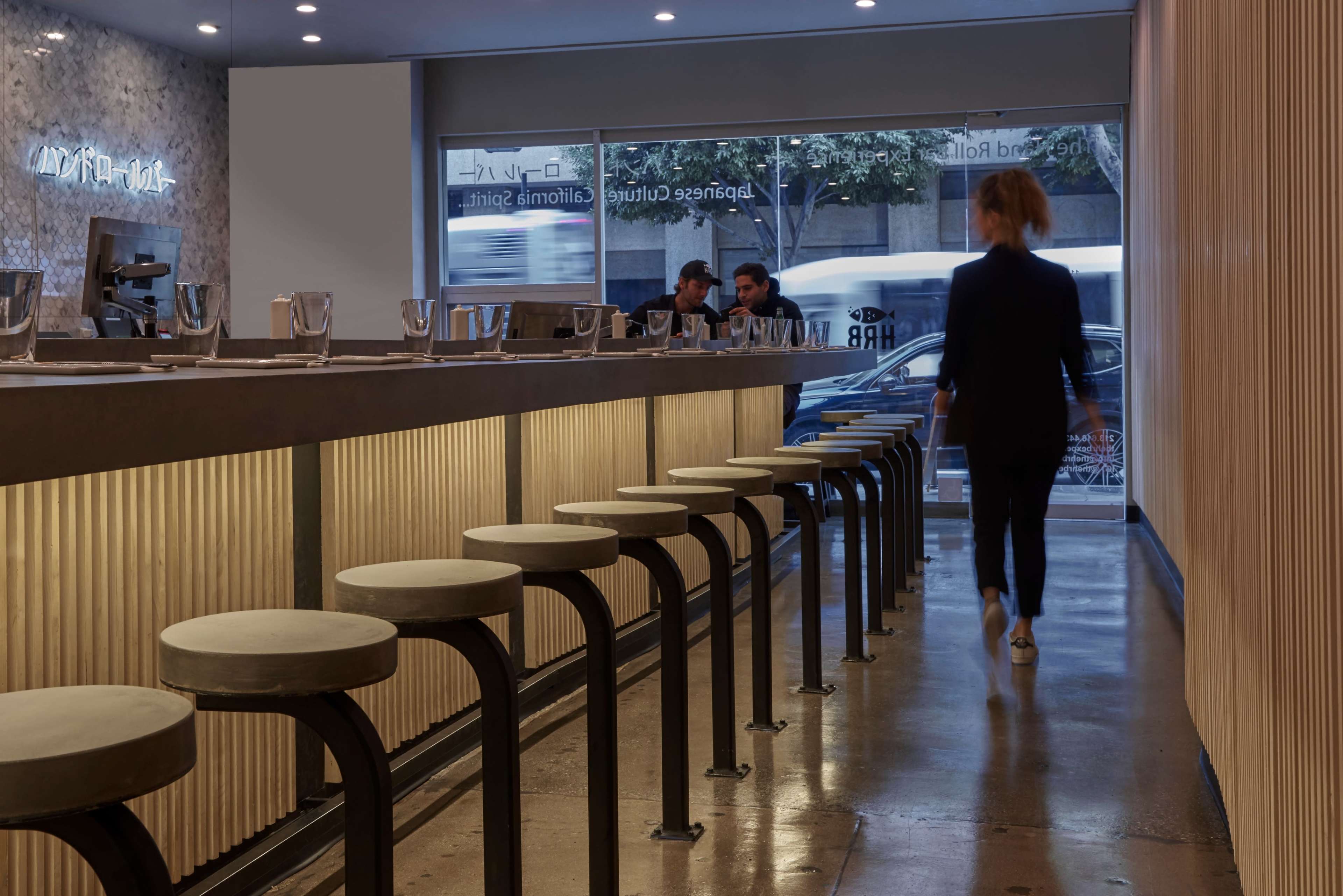 A person walks past a row of modern bar stools in a minimalist café with a light-colored interior.