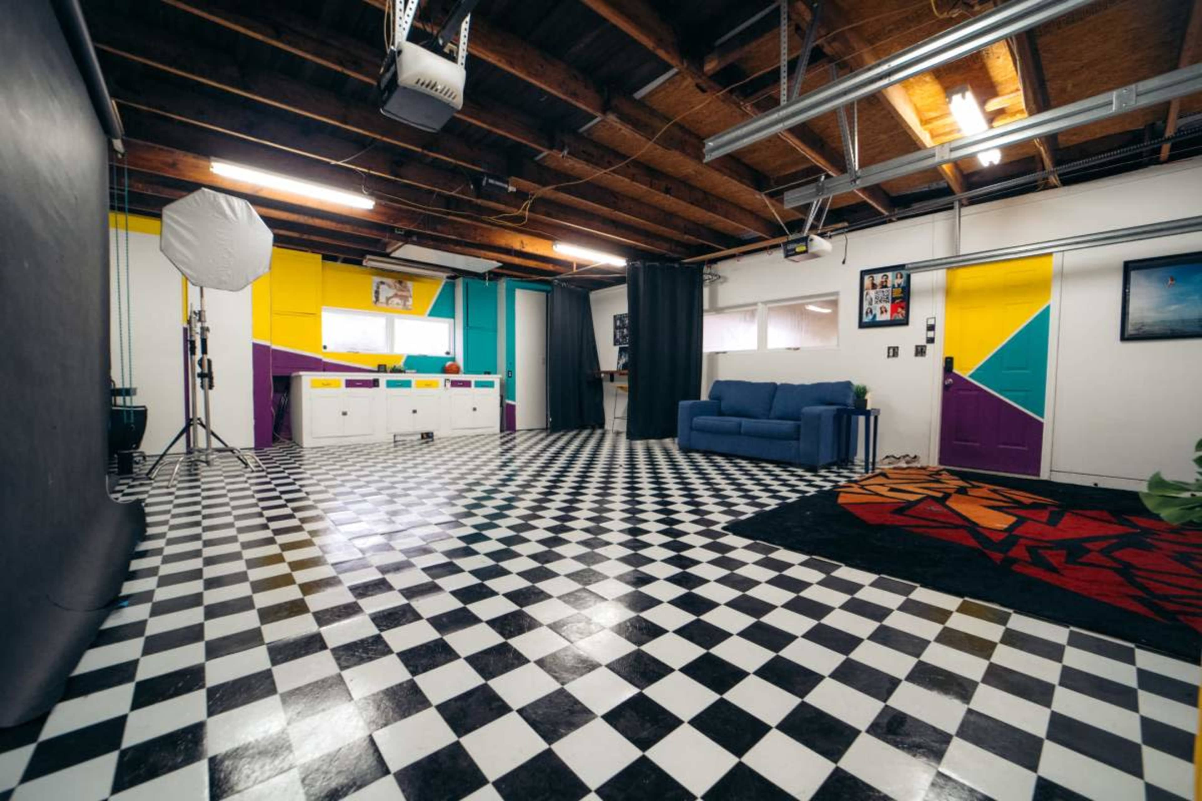 A spacious room with a checkered black and white floor, colorful walls, a blue couch, and photography equipment set up in one corner.