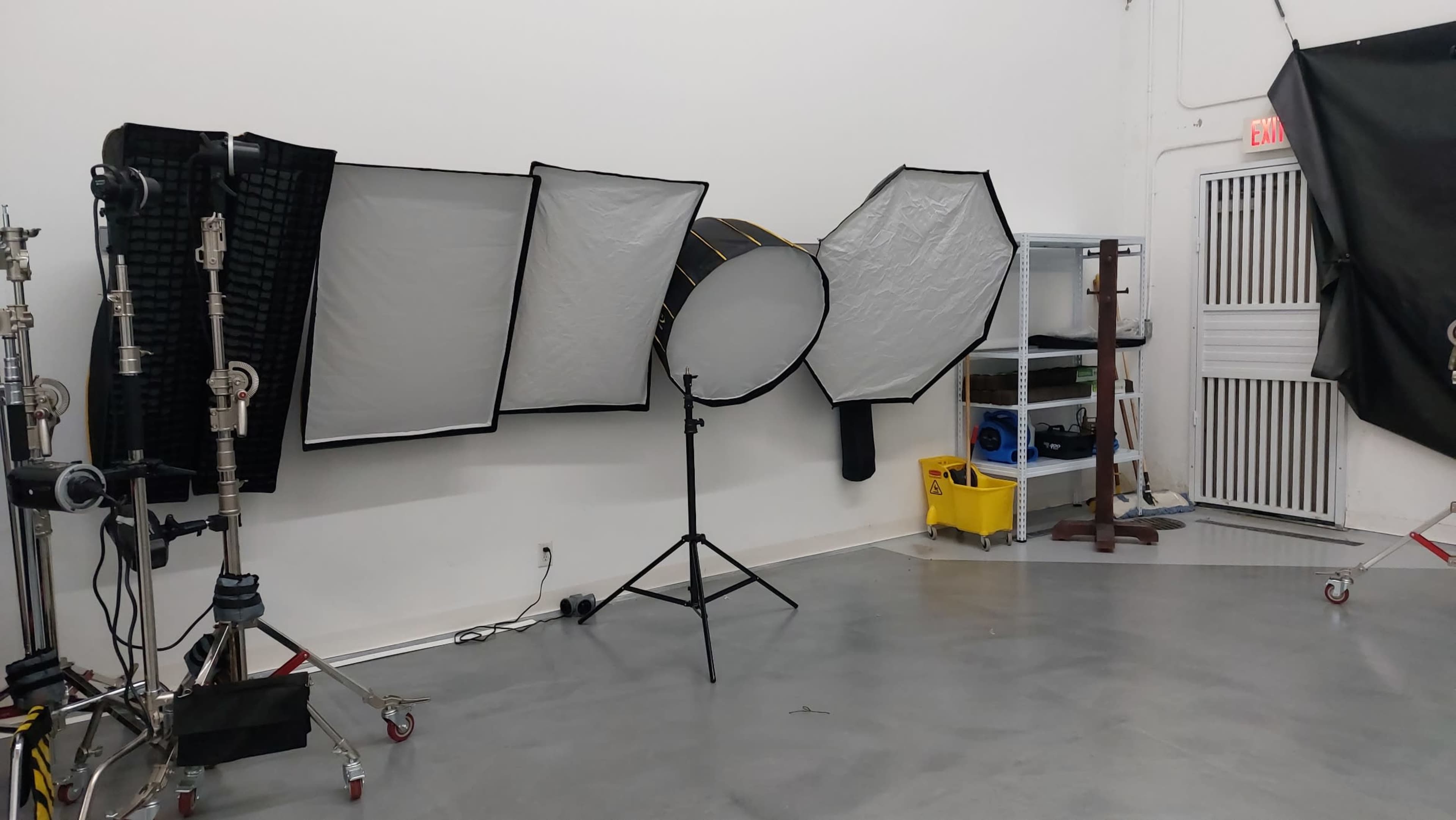 The image shows a photography studio with various lighting equipment and a shelving unit in a brightly lit room.