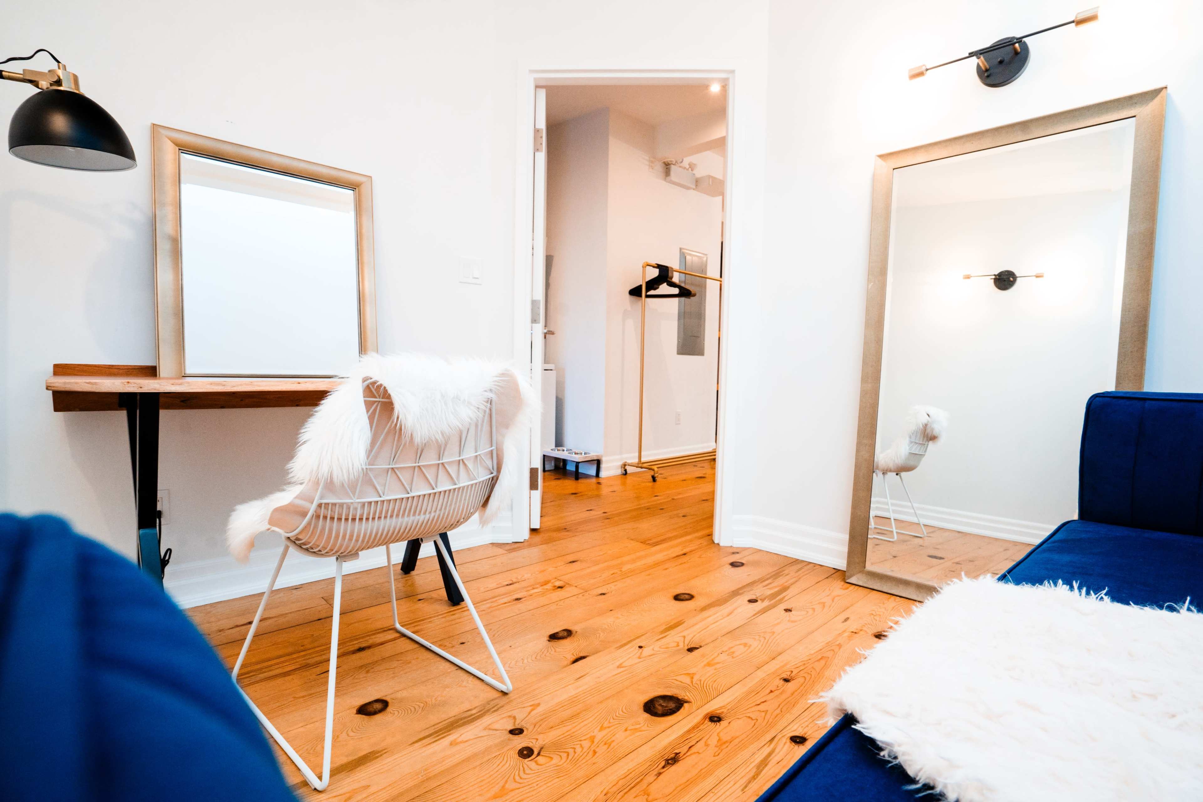 A bright, modern room featuring a wooden floor, a desk with a chair, two large mirrors, and a blue sofa.