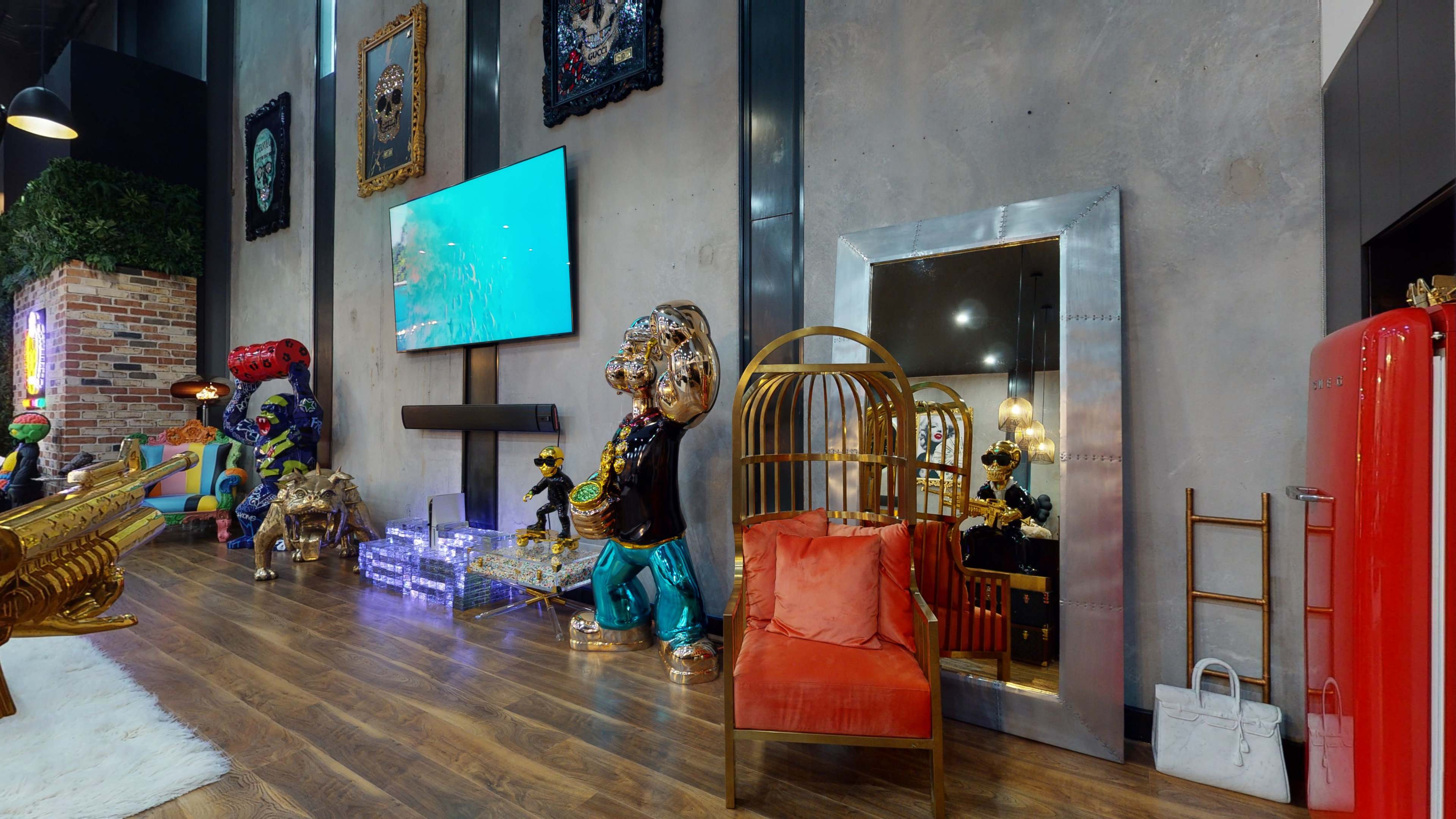 The image features a modern interior with eclectic decor, including colorful statues, a large television, a decorative mirror, and a red refrigerator.