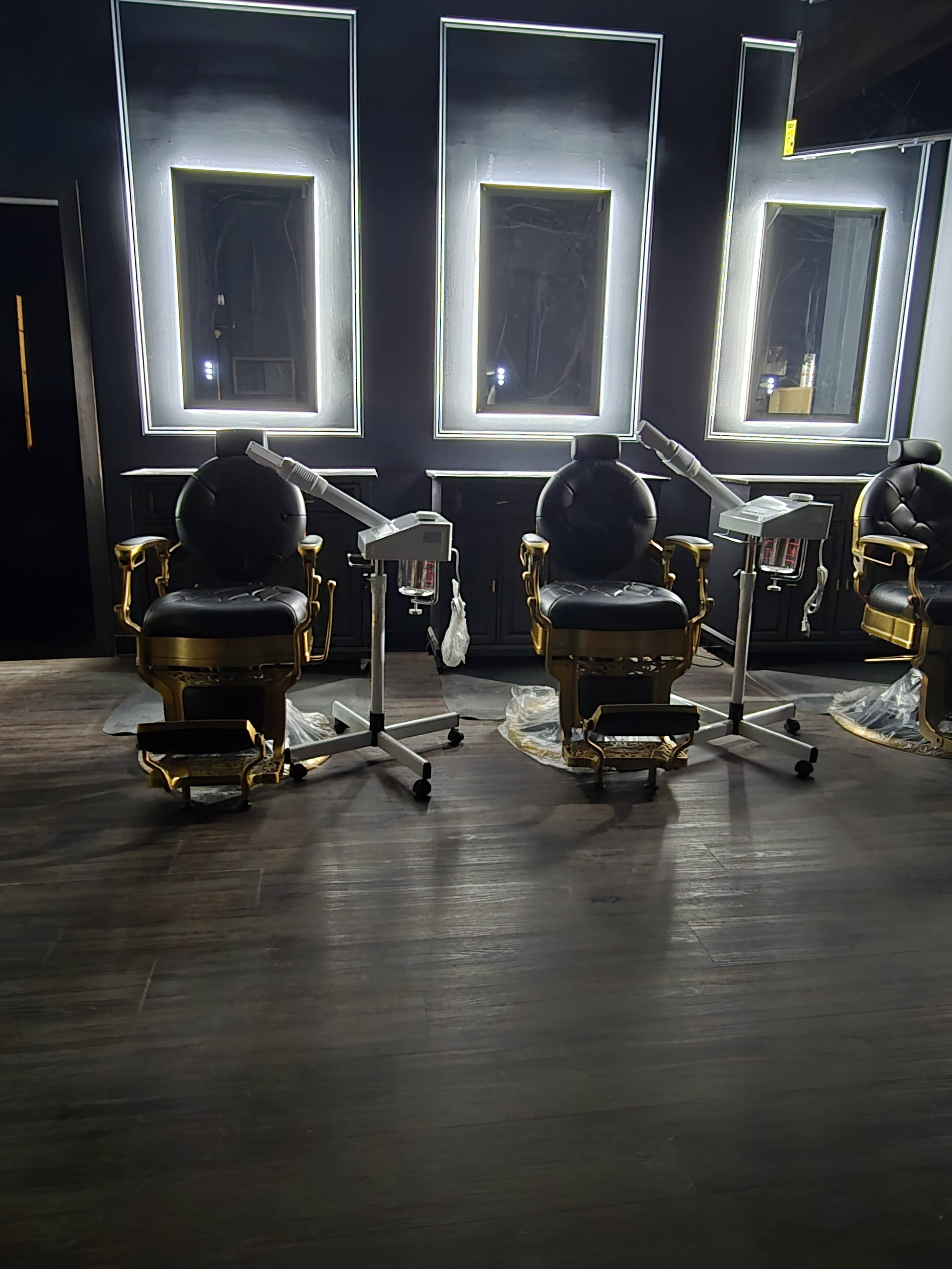 The image shows two black and gold barber chairs positioned in front of illuminated mirrors in a dimly lit interior.