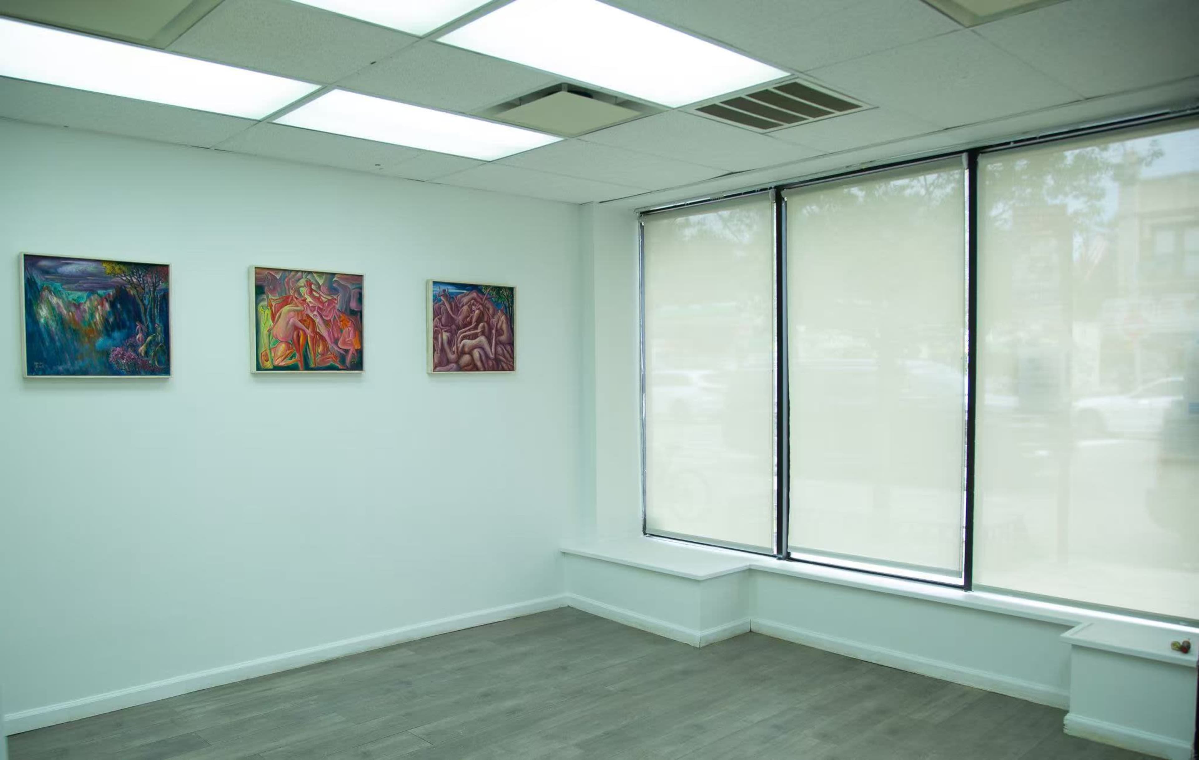 The room features three framed artworks on the wall, with a large window partially covered by blinds allowing light to enter.