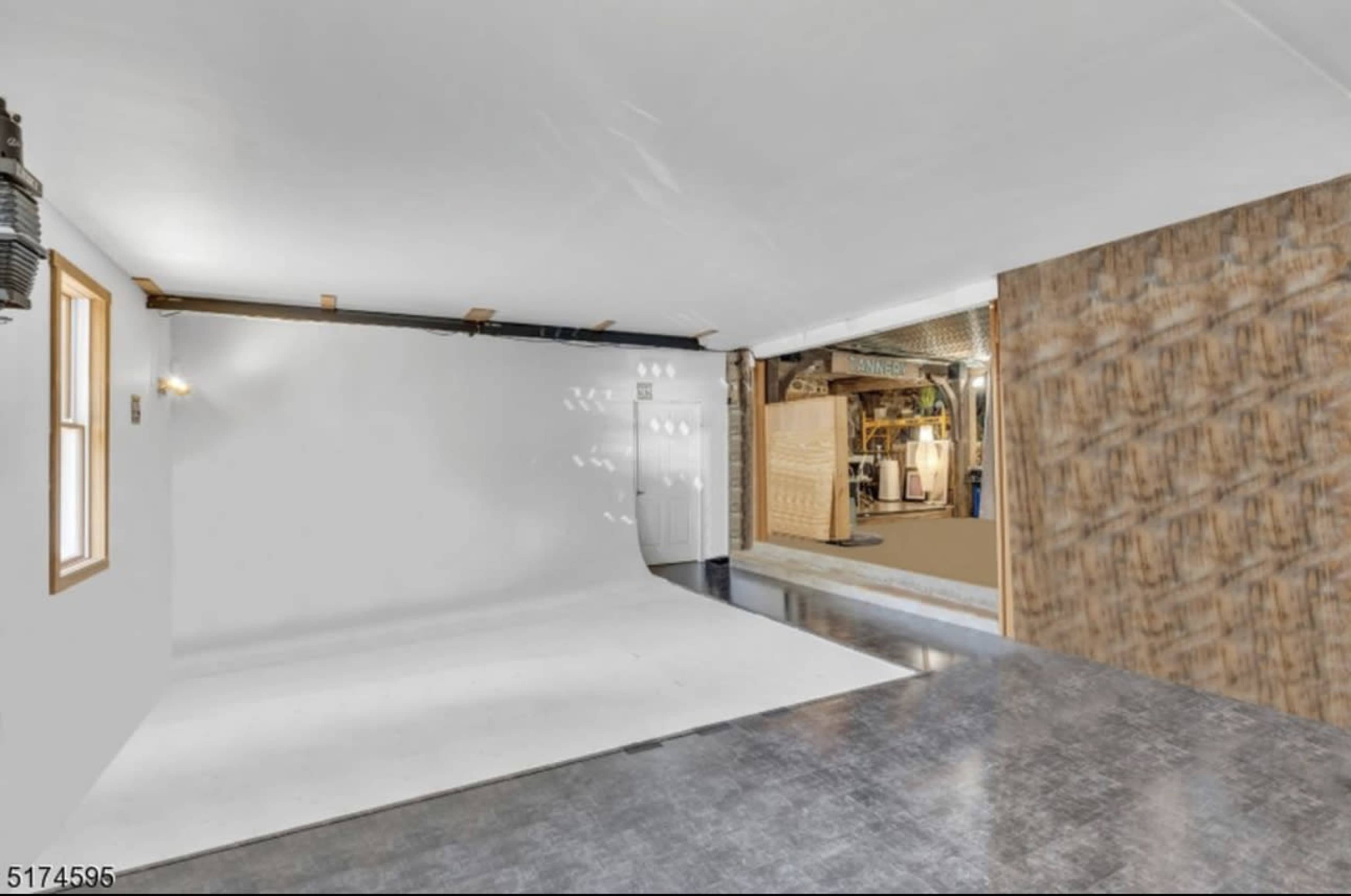 The image shows a spacious room with a white backdrop on one side and a textured wall on the other, featuring a concrete floor and exposed structural elements in the background.