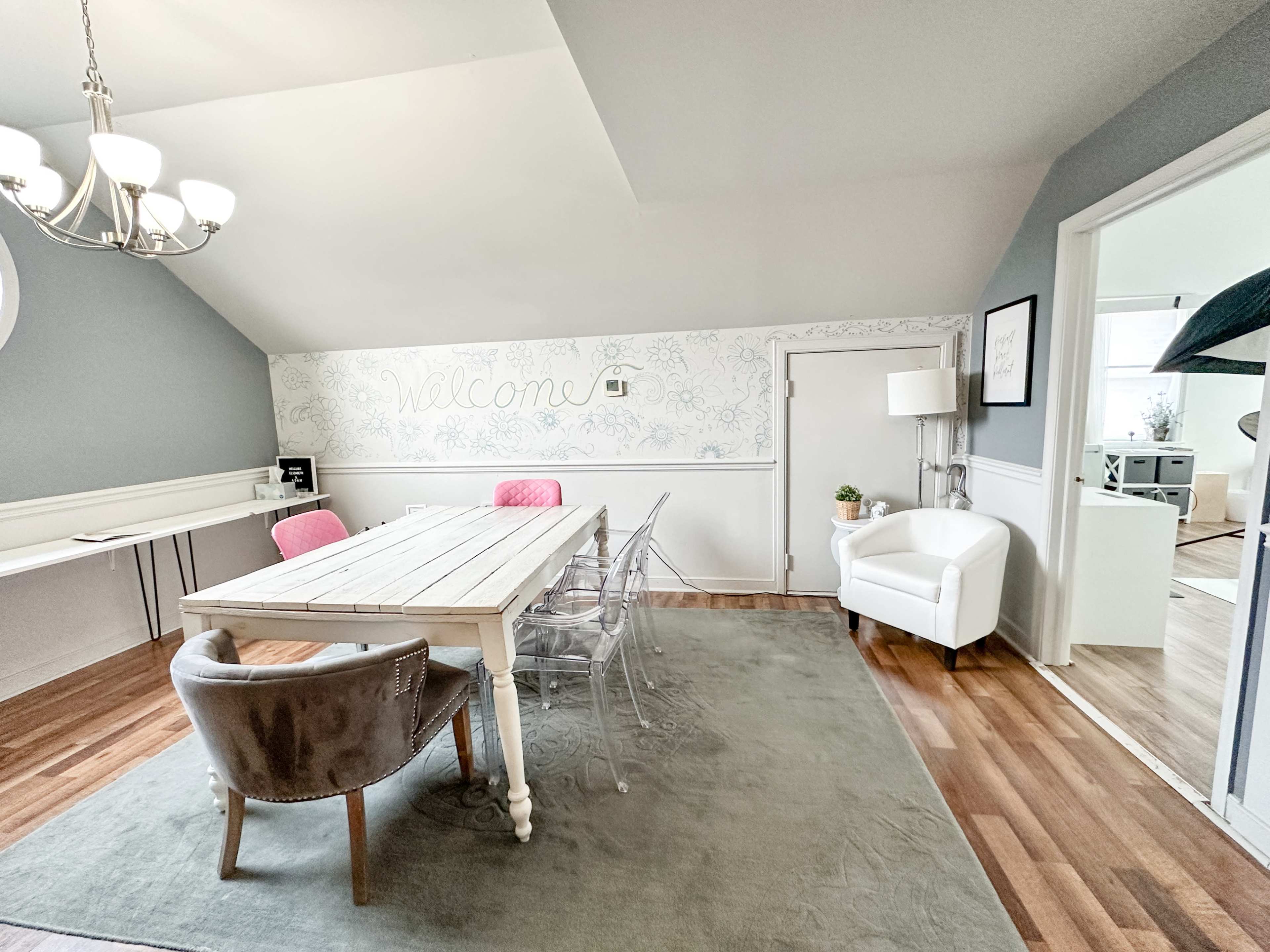 A dining area with a white table, clear chairs, a gray area rug, and a welcoming wall with decorative elements.