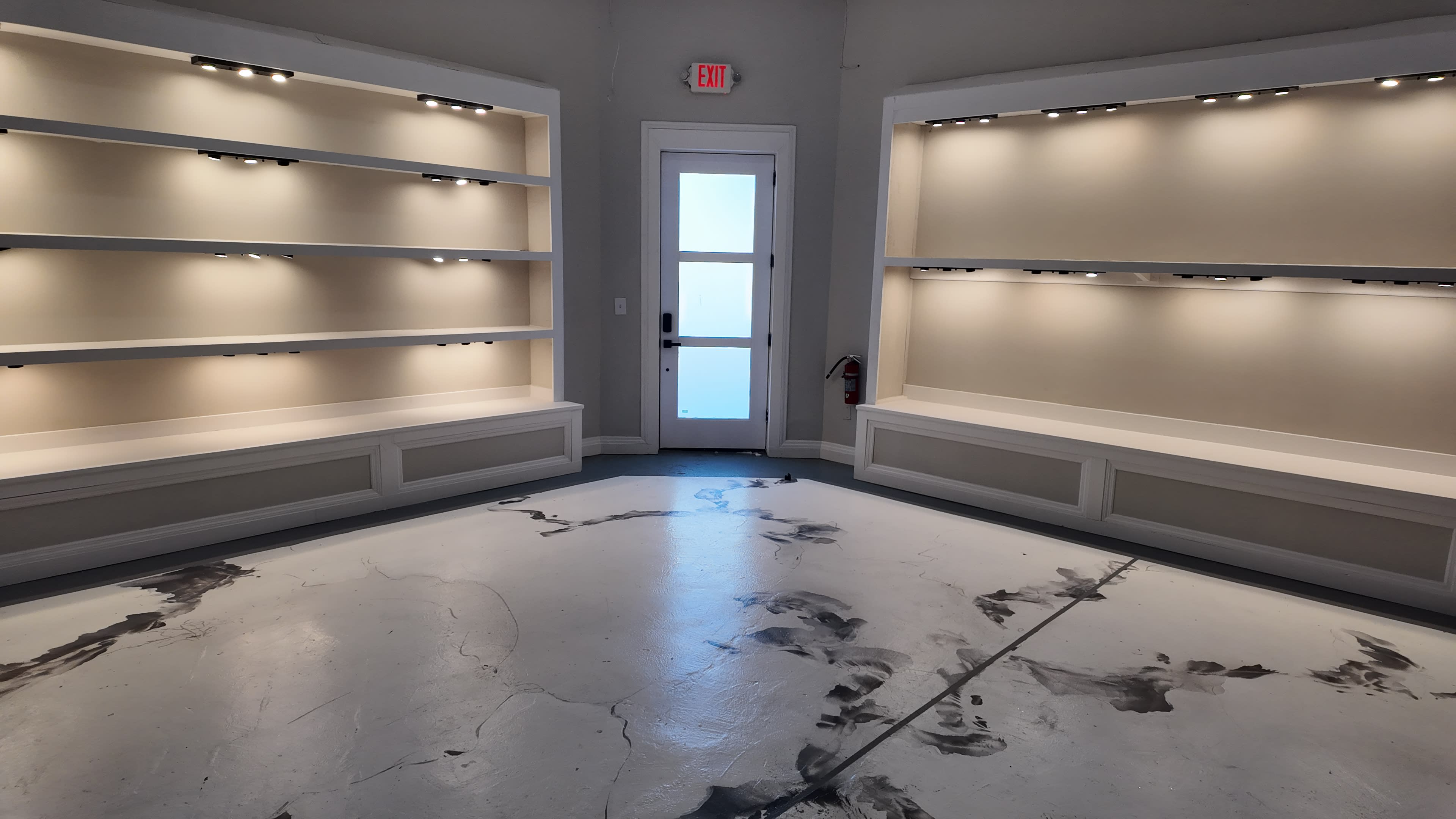 The image shows a minimalist room with blank shelves on two walls and a door in the center.