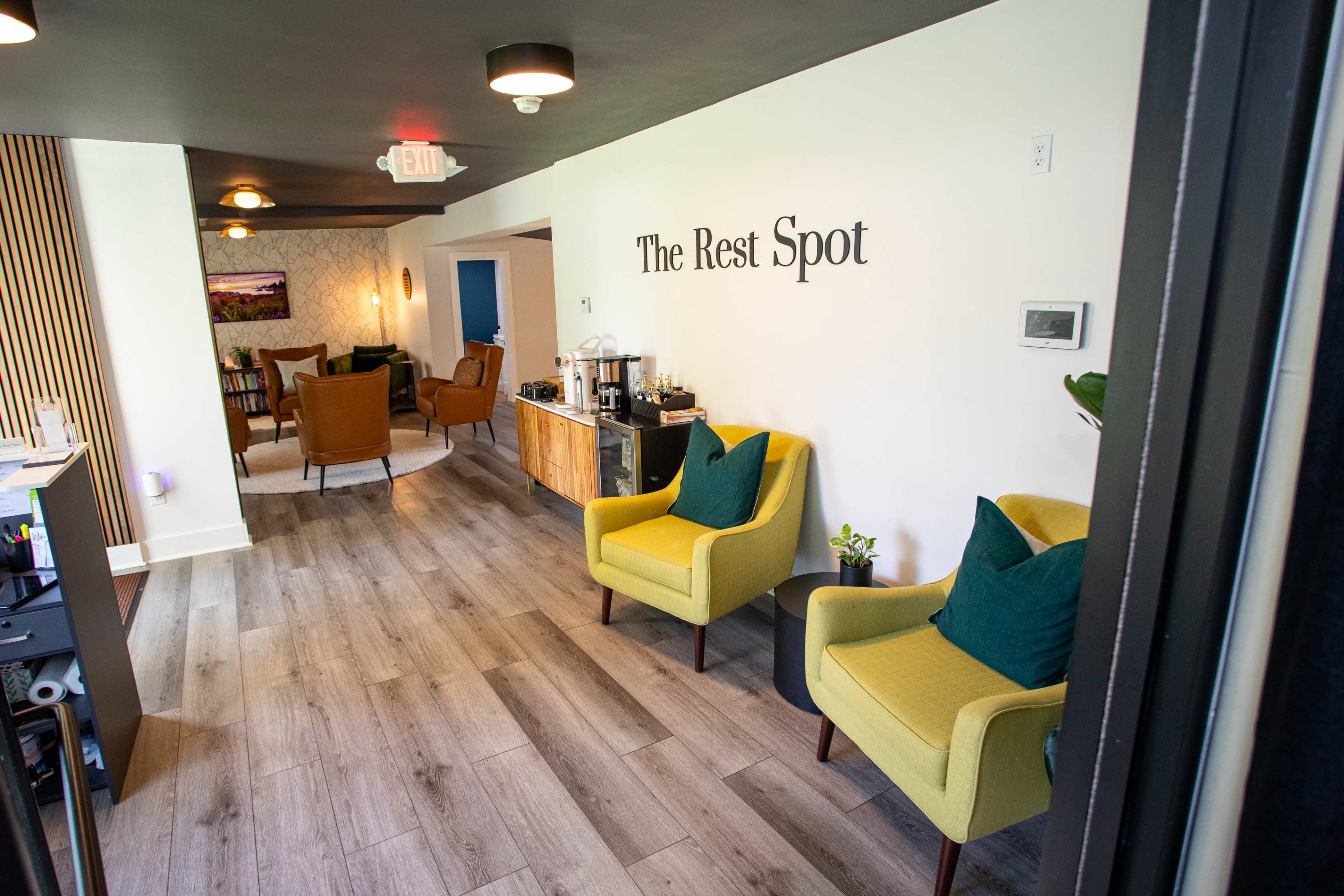 The image shows a modern interior space titled "The Rest Spot," featuring yellow armchairs, a coffee station, and a welcoming seating area with plants and decorative elements.