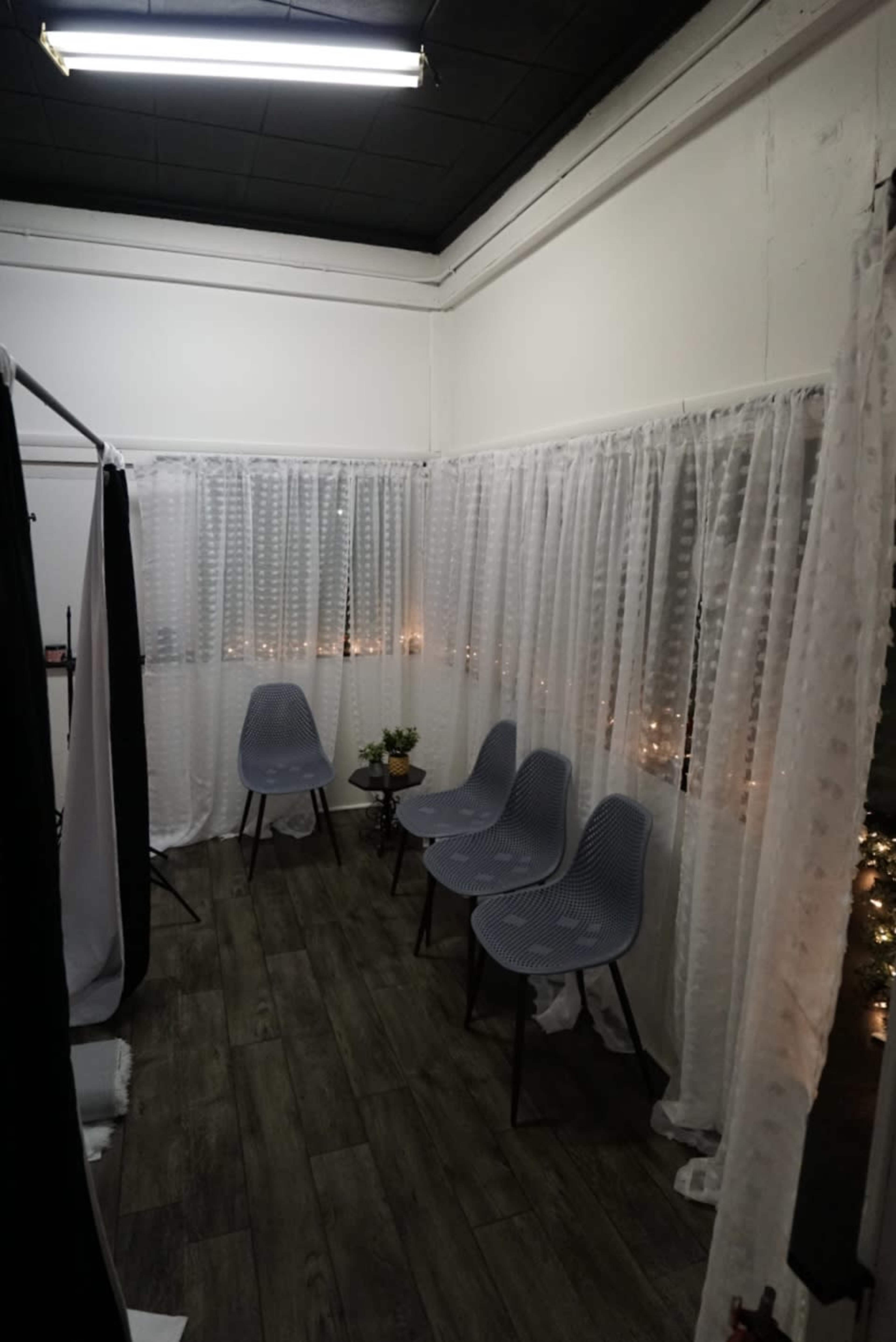 A small room with four gray chairs, white sheer curtains along the walls, and a few decorative plants on a table.