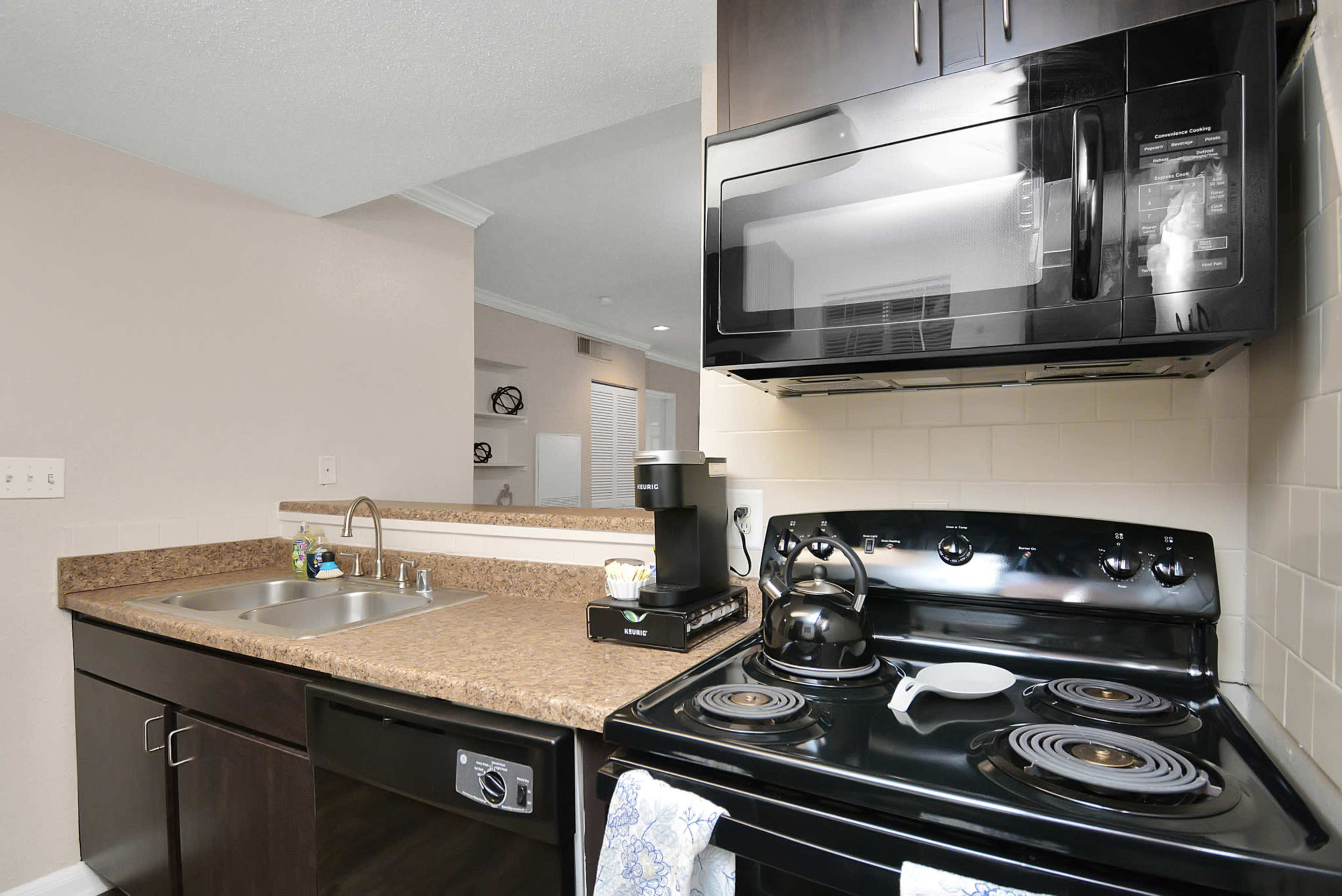 A kitchen with dark cabinets, a black stove and microwave, a stainless steel sink, and a coffee maker on the countertop.