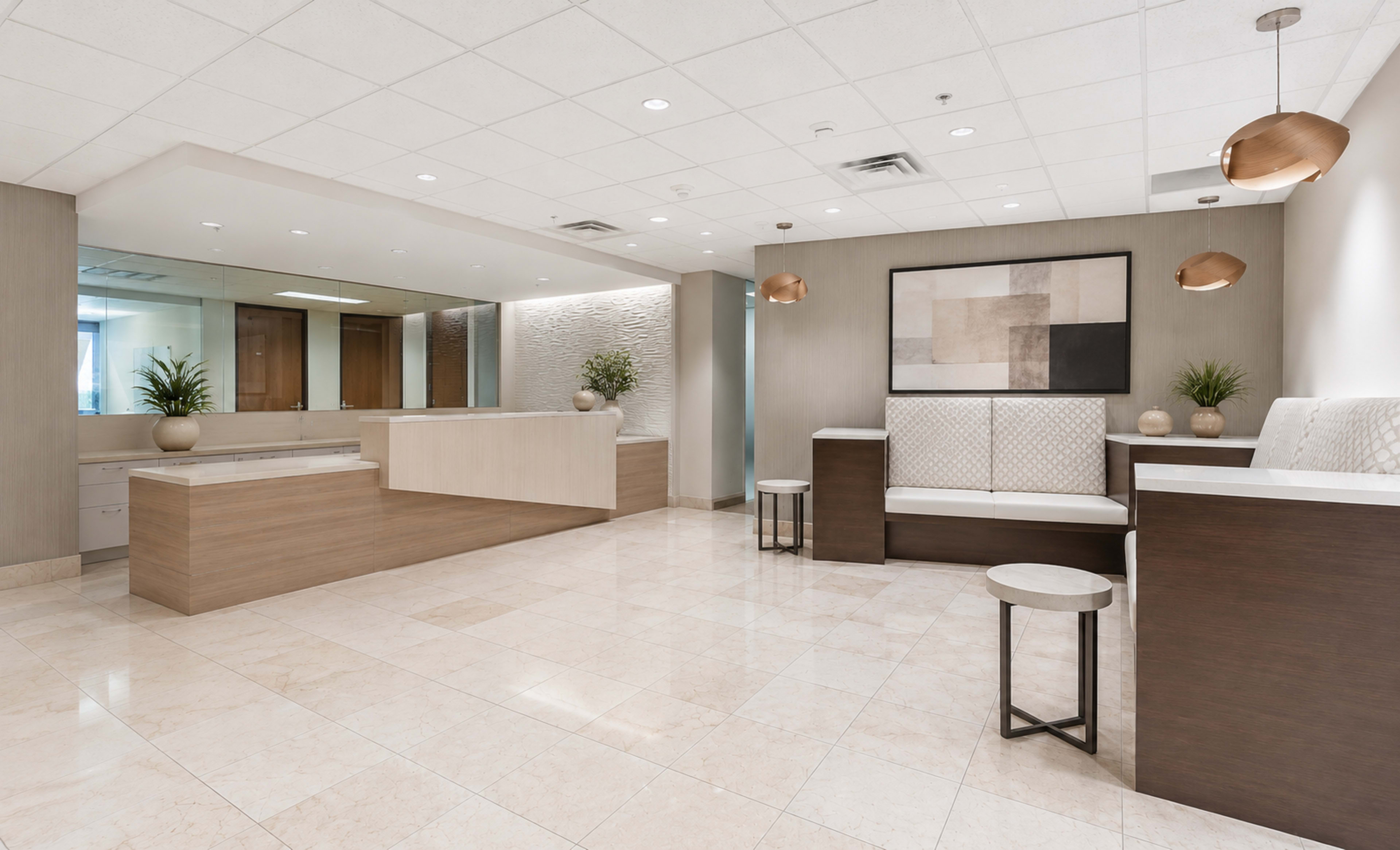 The image shows a modern reception area with a light-colored marble floor, a wooden reception desk, seating areas, and decorative plants.