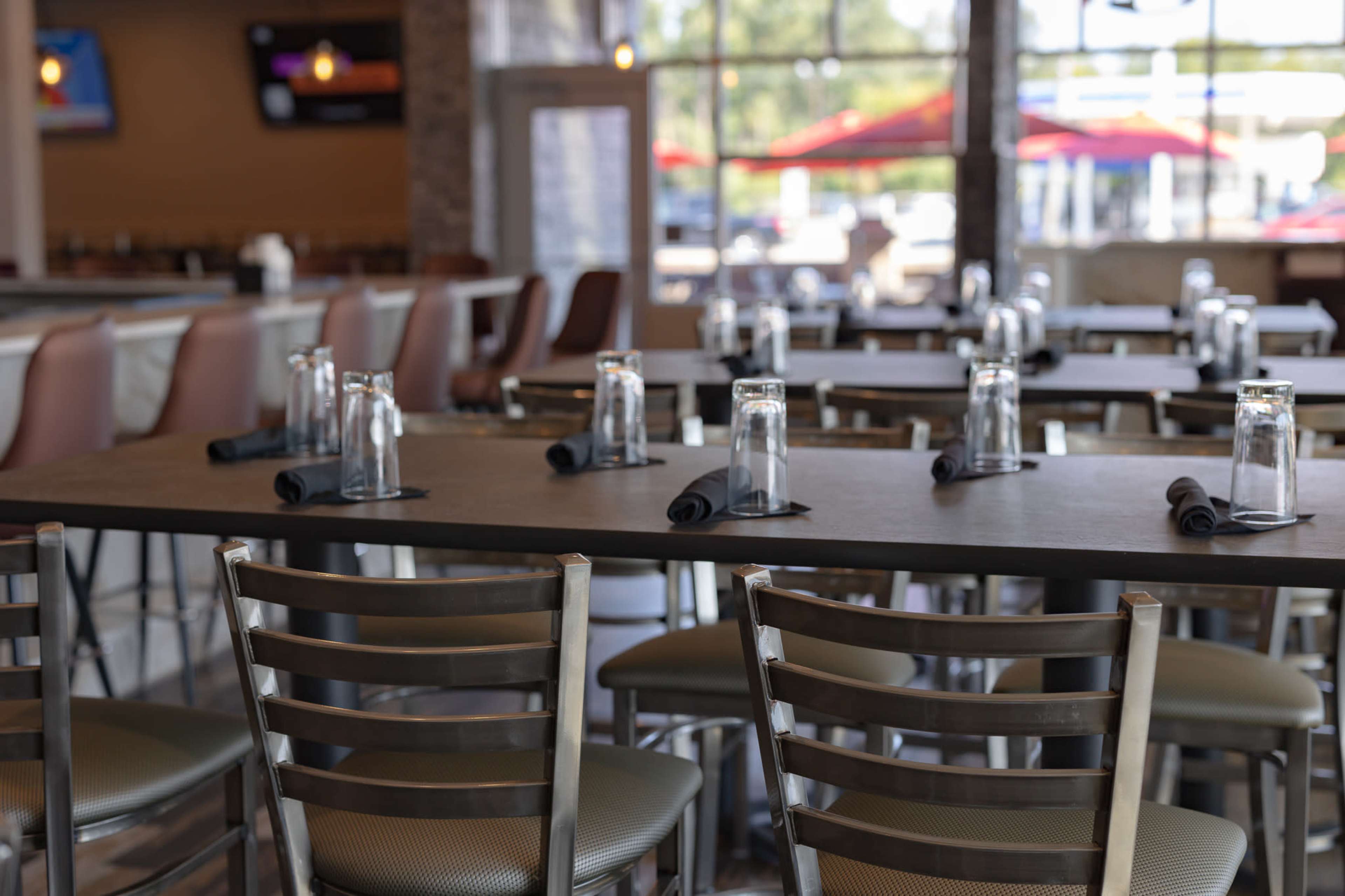 A dining area features metal chairs and a long table set with water glasses and napkins.