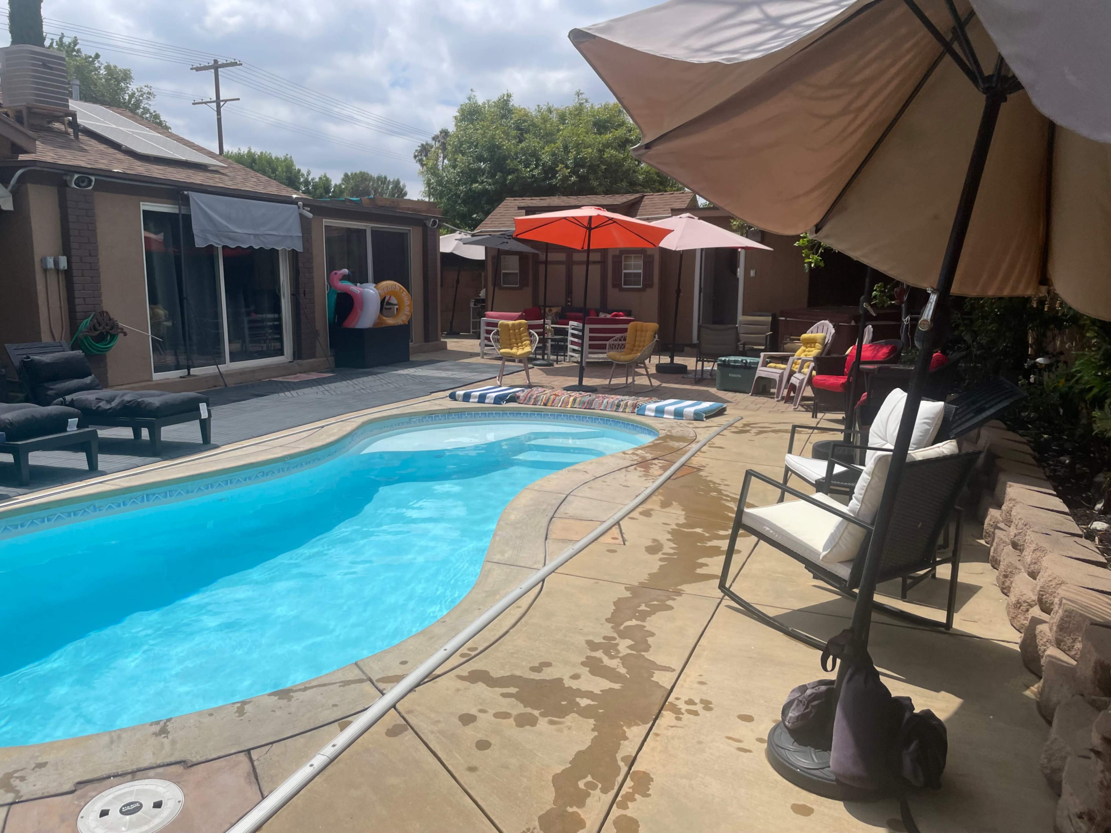 The image shows a backyard with a swimming pool surrounded by lounge chairs, umbrellas, and a patio area.