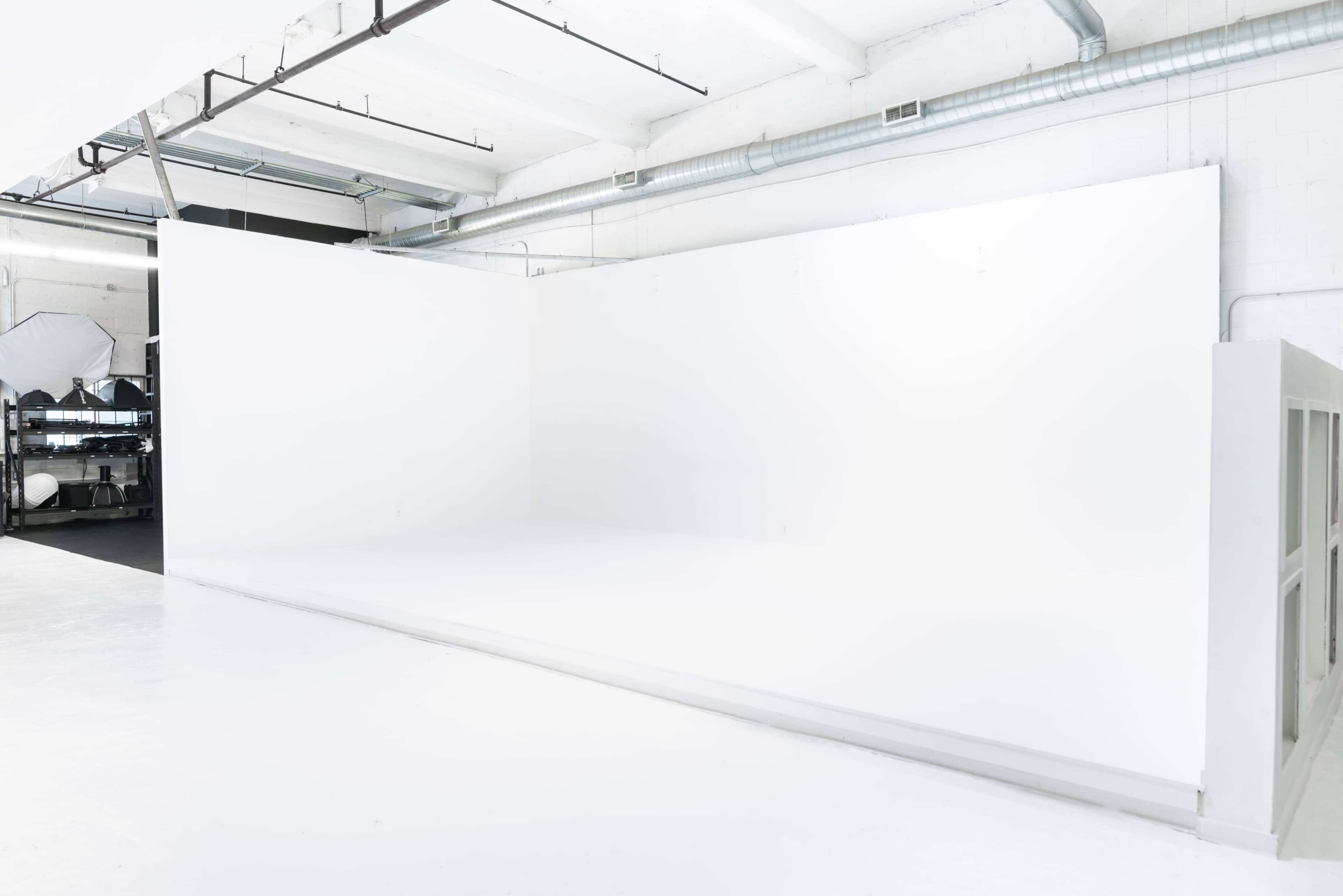 The image shows a spacious, minimalistic white studio with plain walls and a polished floor.