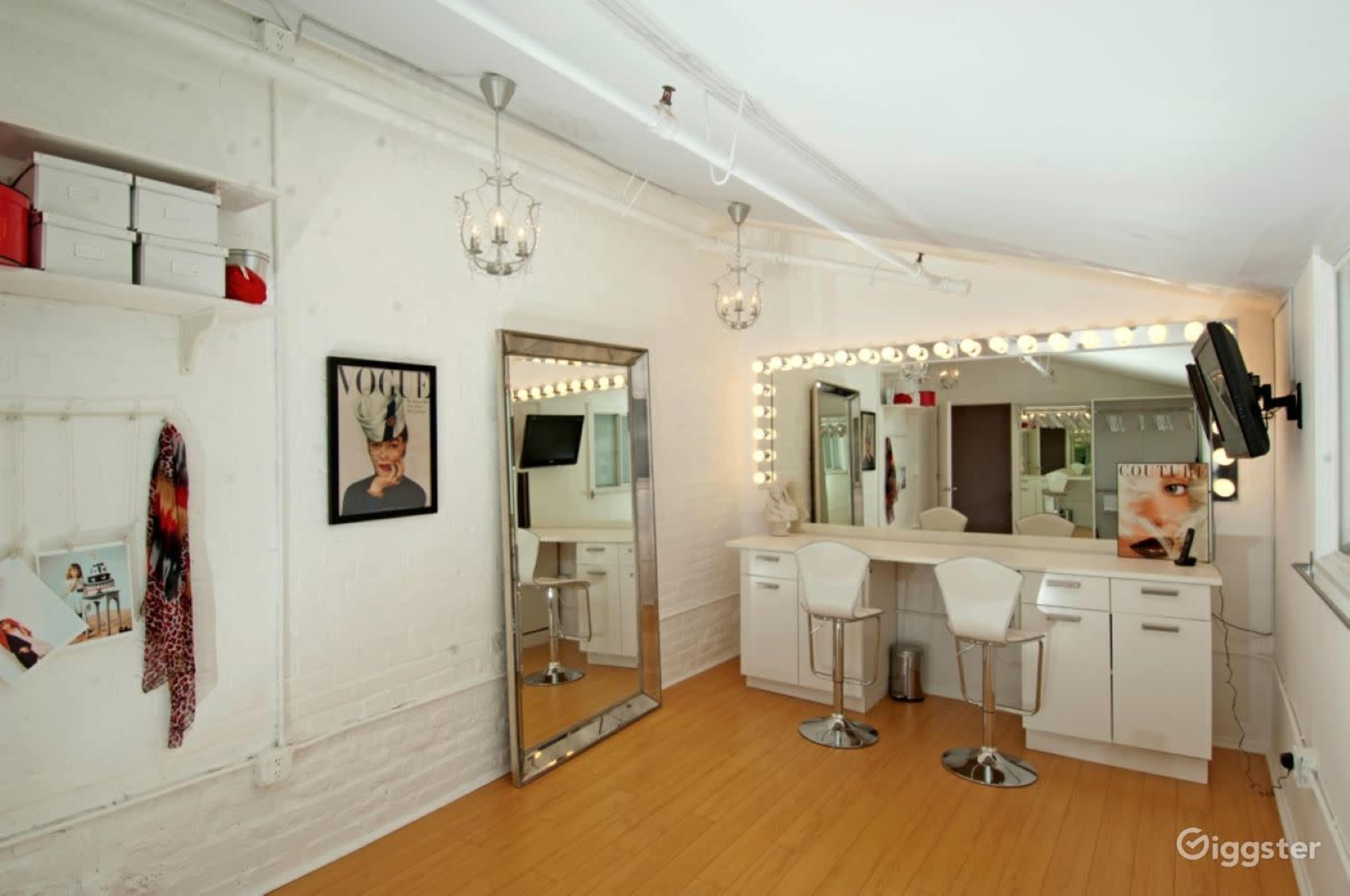A well-lit makeup room featuring a large mirror with vanity lights, white cabinetry, and two modern bar stools.