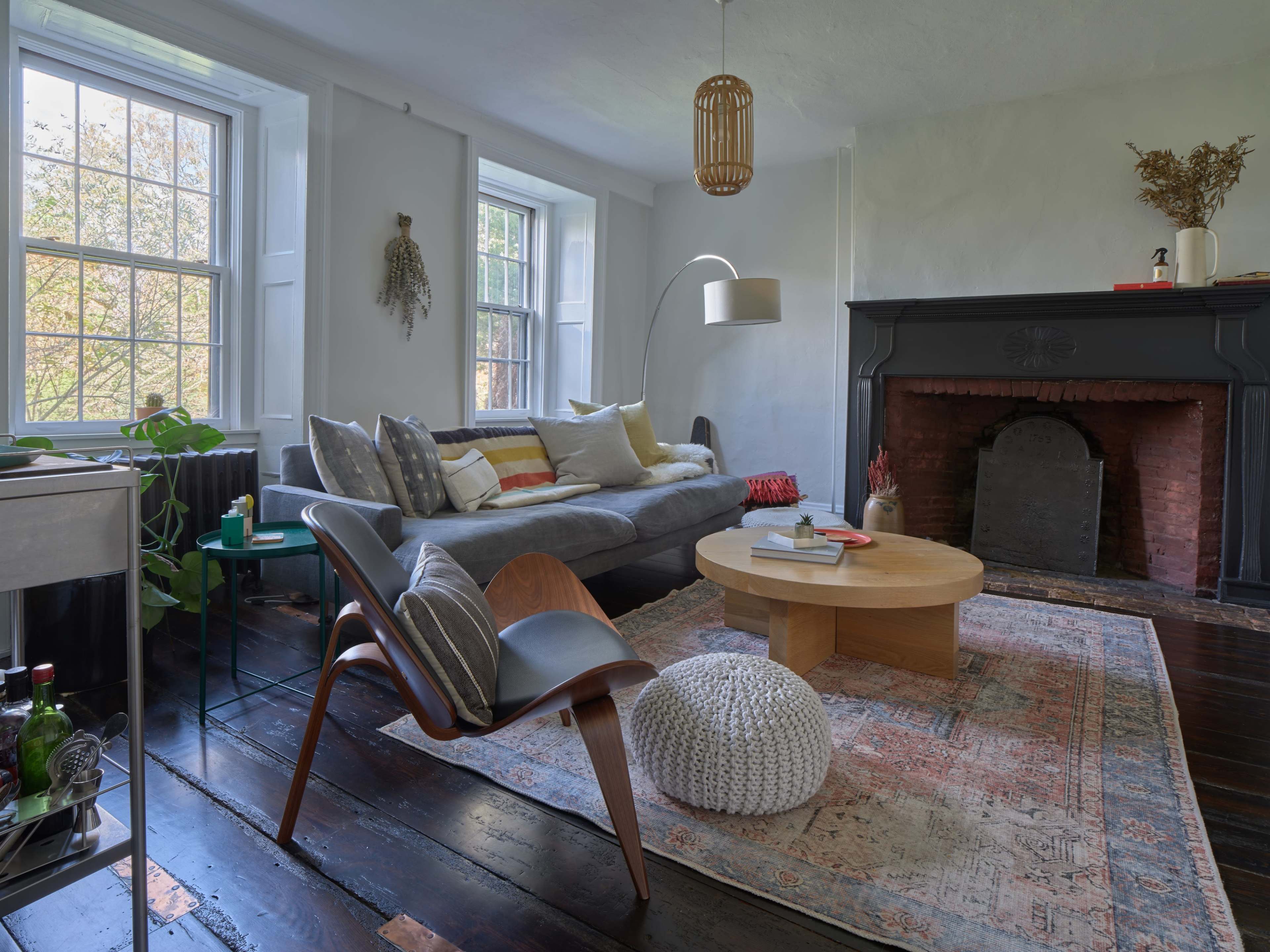 A cozy living room with a gray sofa, a round wooden coffee table, a patterned rug, and a fireplace with a dark mantel.