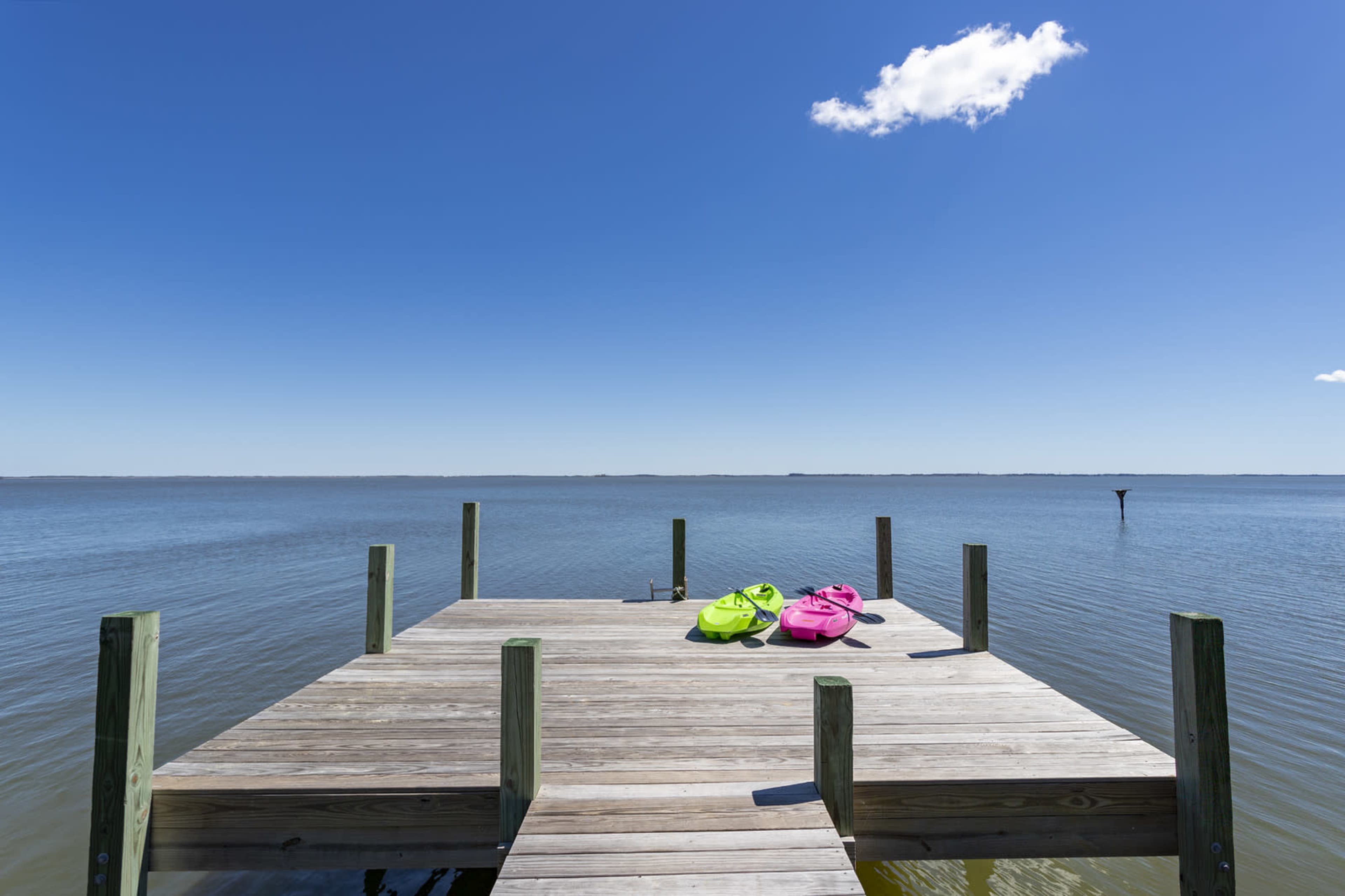 A wooden dock extends over calm water, with two kayaks resting on it under a clear blue sky.