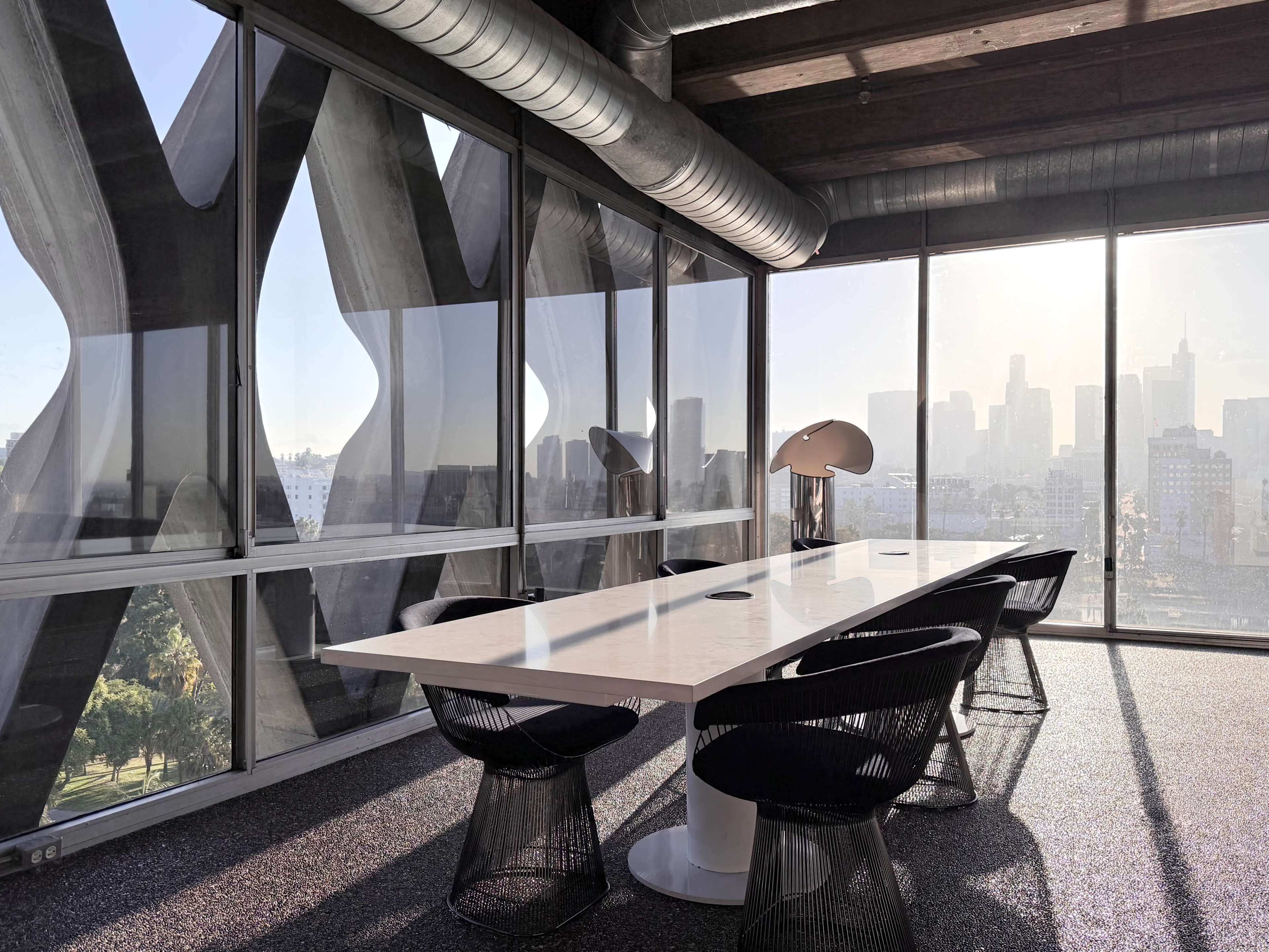 The image shows a modern conference room with a white table, black chairs, and large windows overlooking a city skyline illuminated by sunlight.