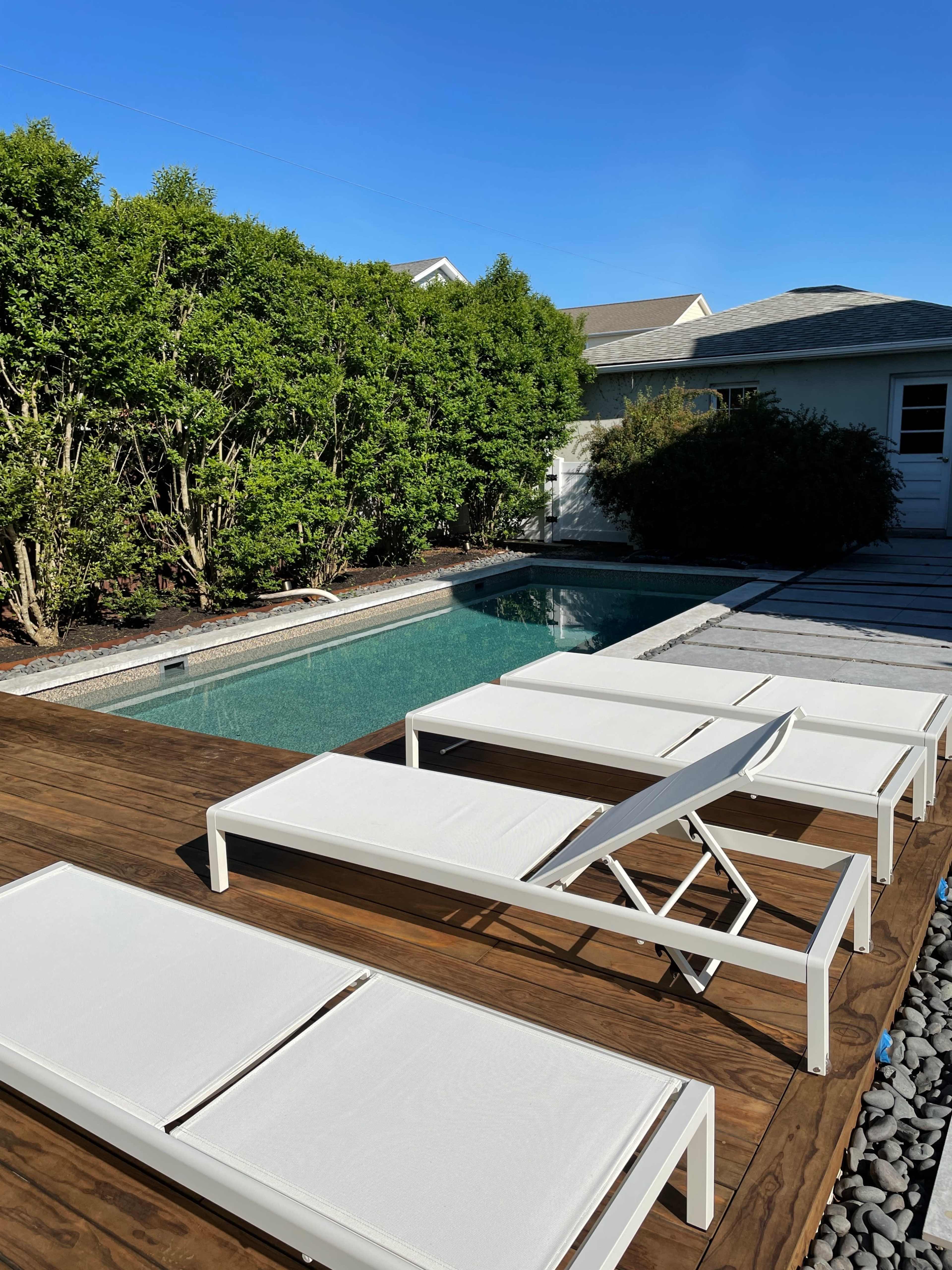 The image shows a backyard with a swimming pool surrounded by wooden decking and white lounge chairs.