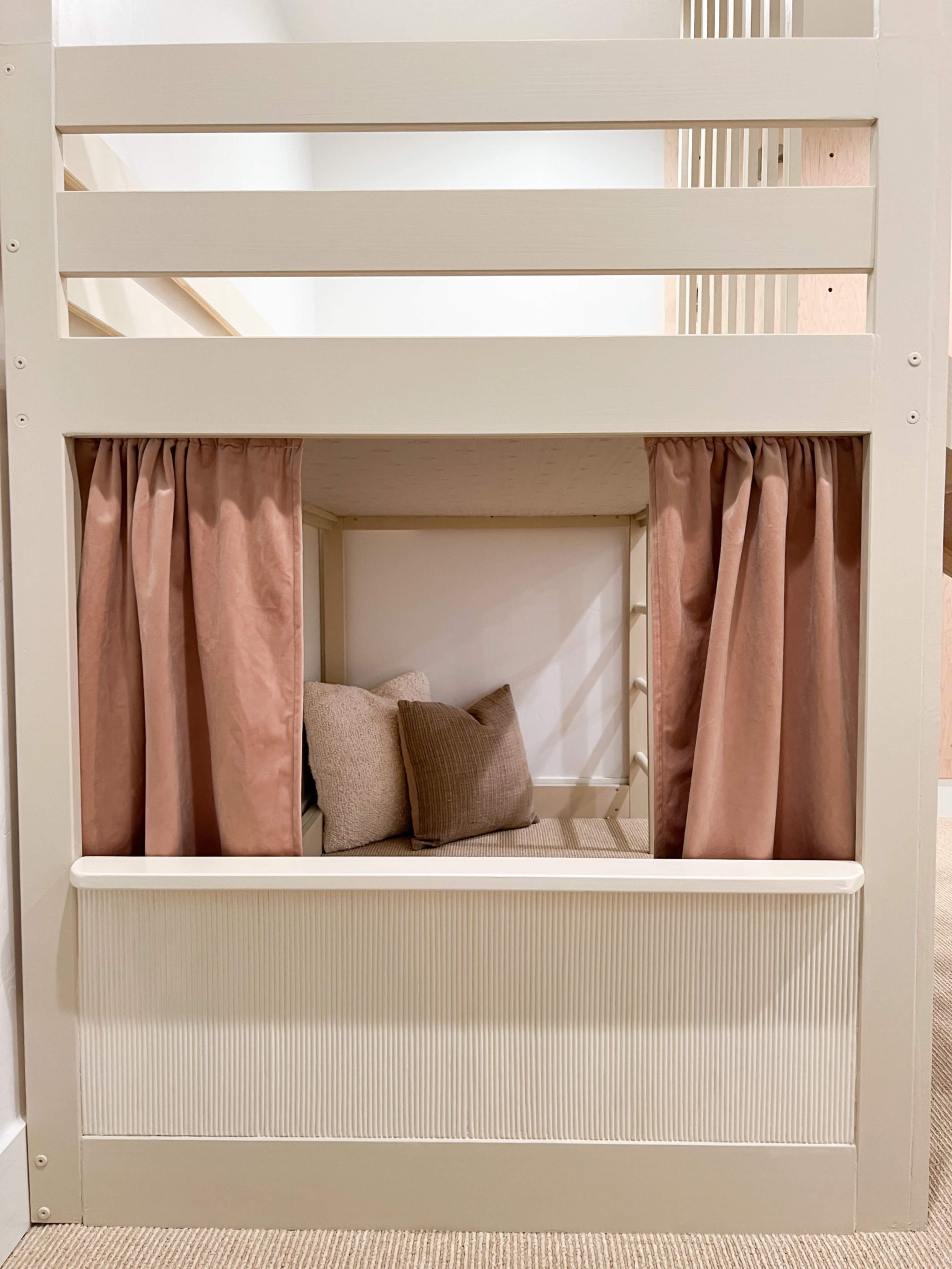 A lofted bed with a cozy, curtained nook underneath containing several cushions.