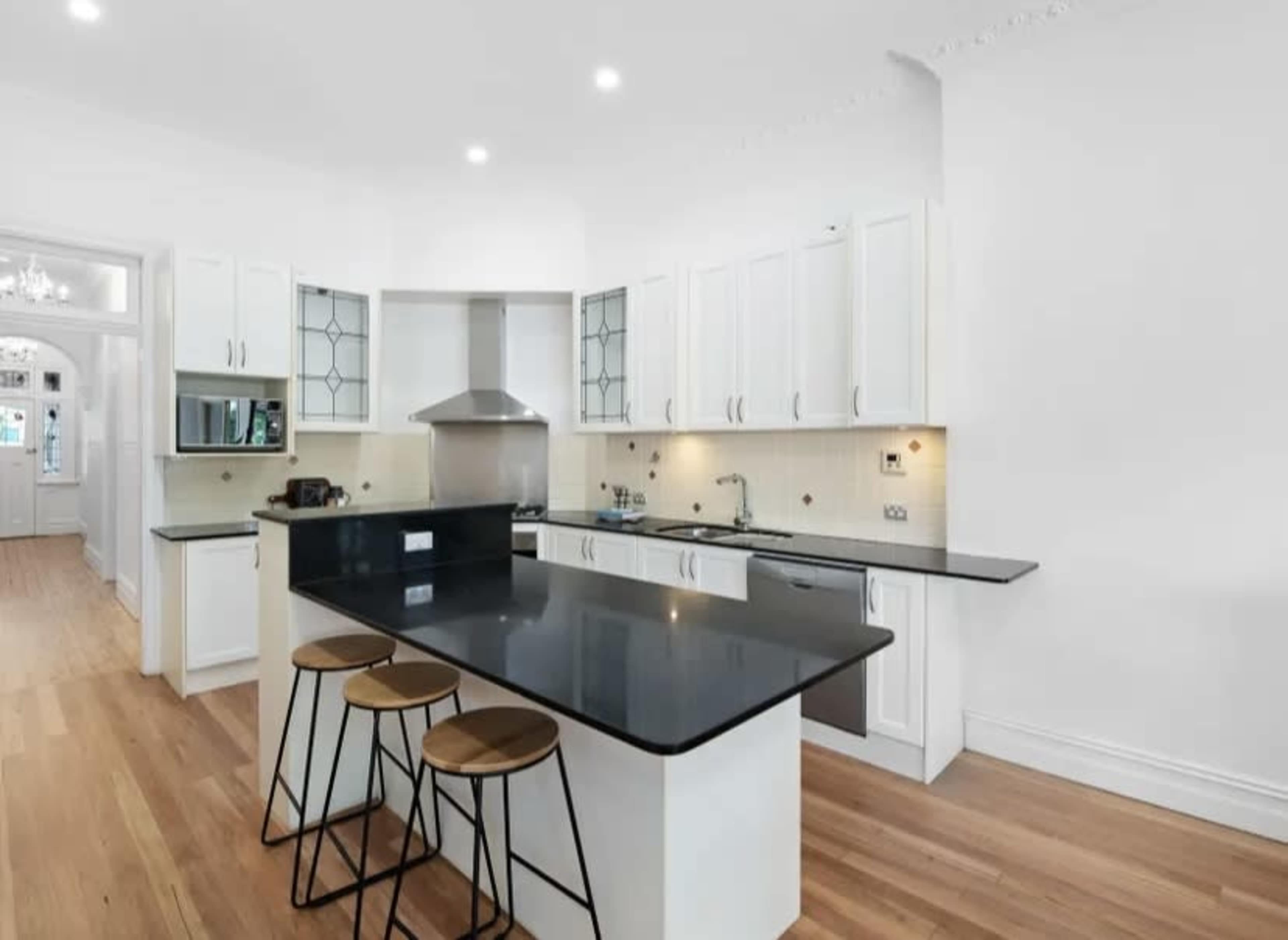 A modern kitchen with white cabinetry, a black countertop, and three wooden bar stools.