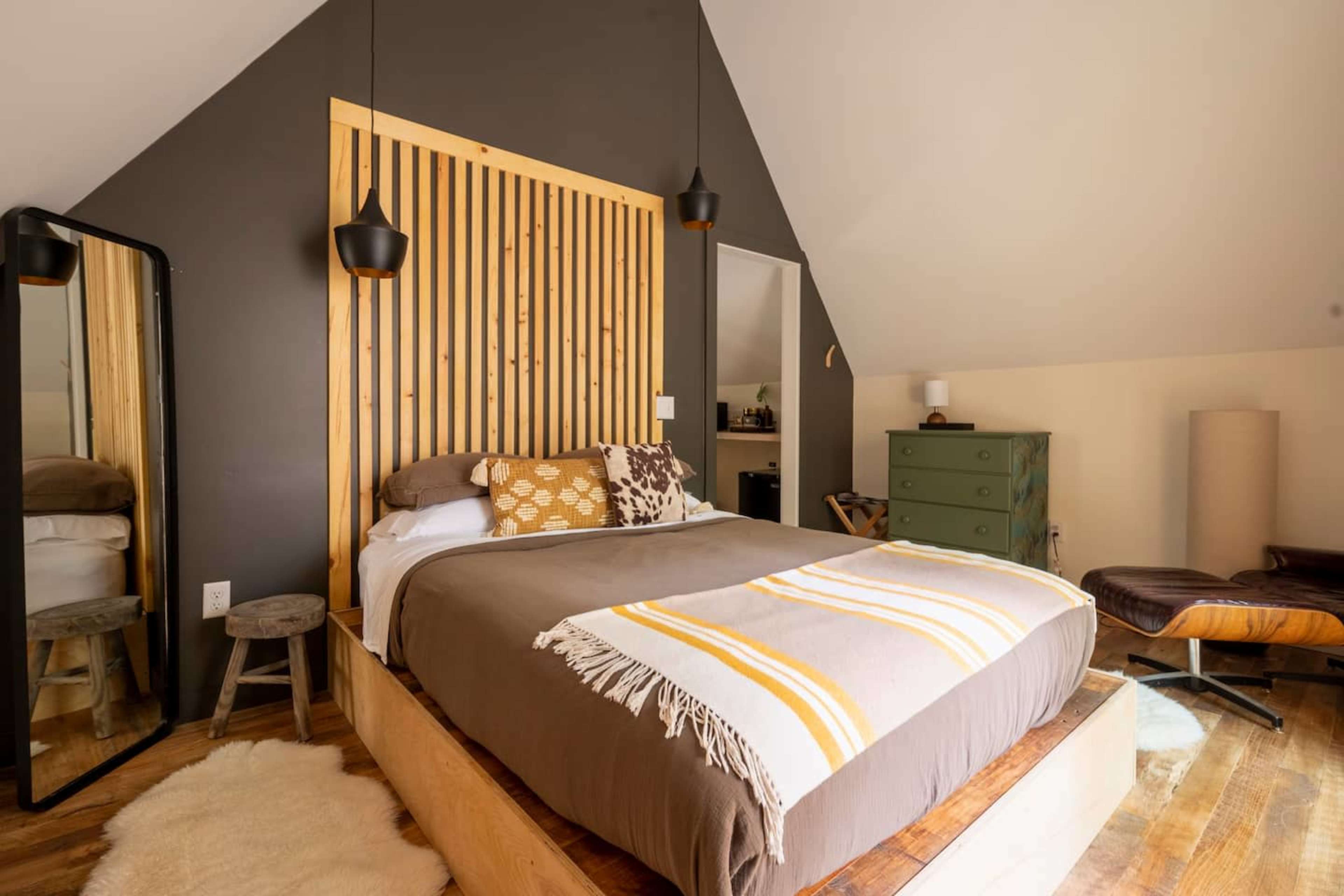 A cozy bedroom featuring a bed with a wooden headboard, a patterned throw, and a large mirror against the wall.