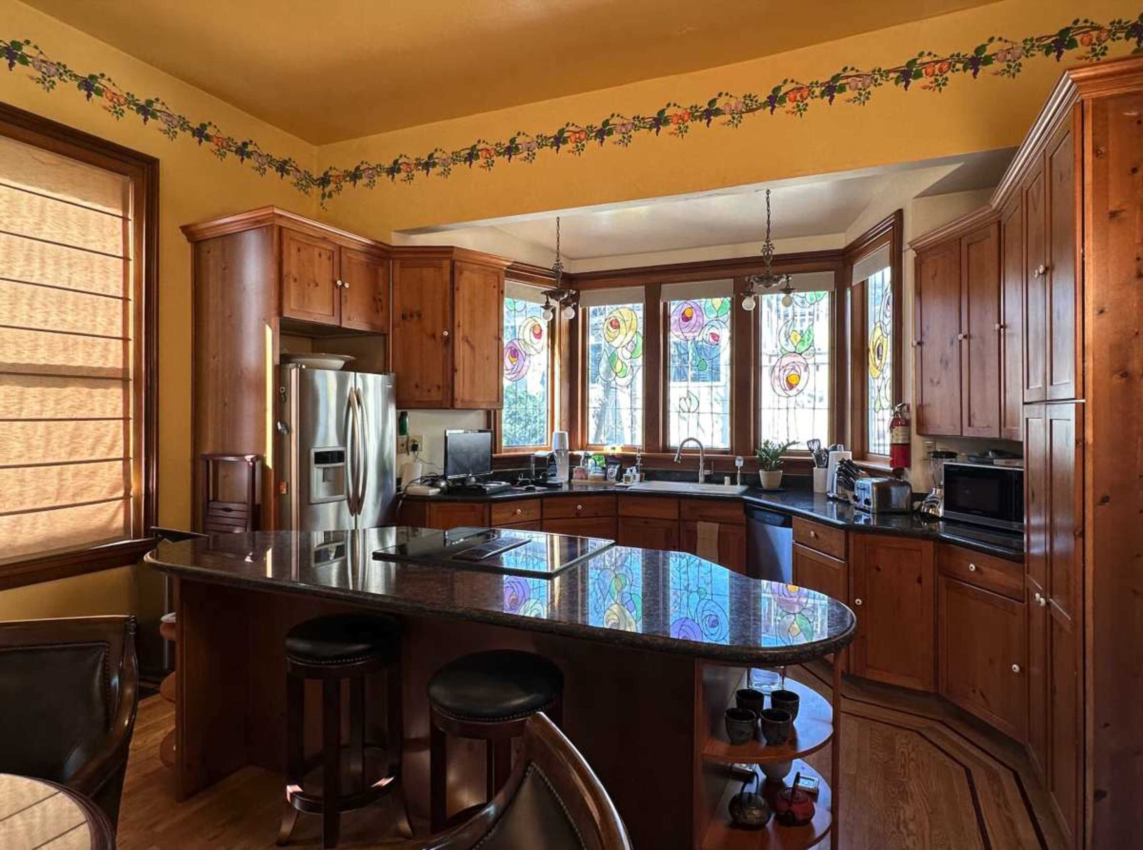 A kitchen featuring wooden cabinets, a dark granite countertop, and large stained glass windows.