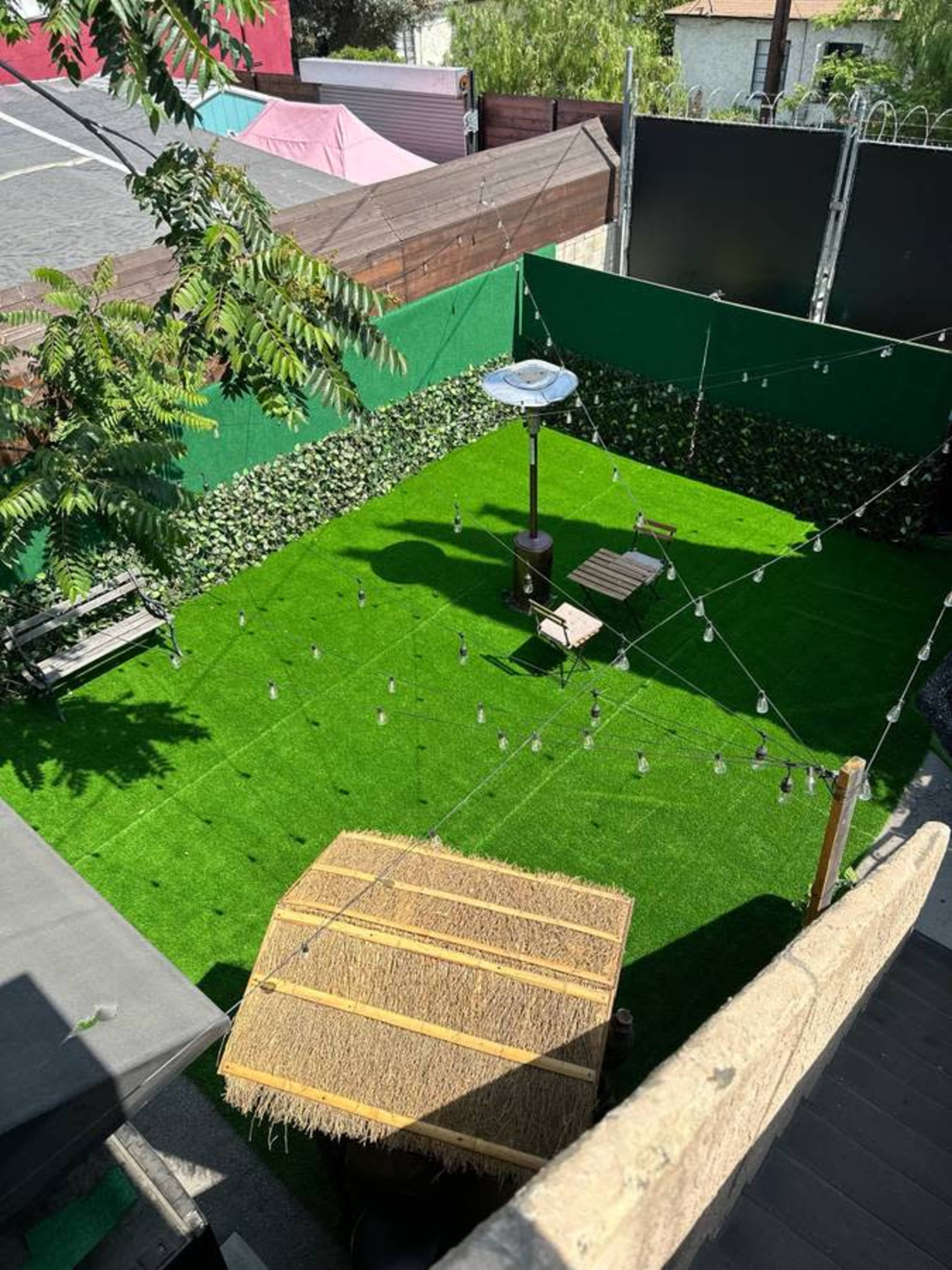 A green artificial turf yard featuring a wooden seating area, a patio heater, and string lights overhead.
