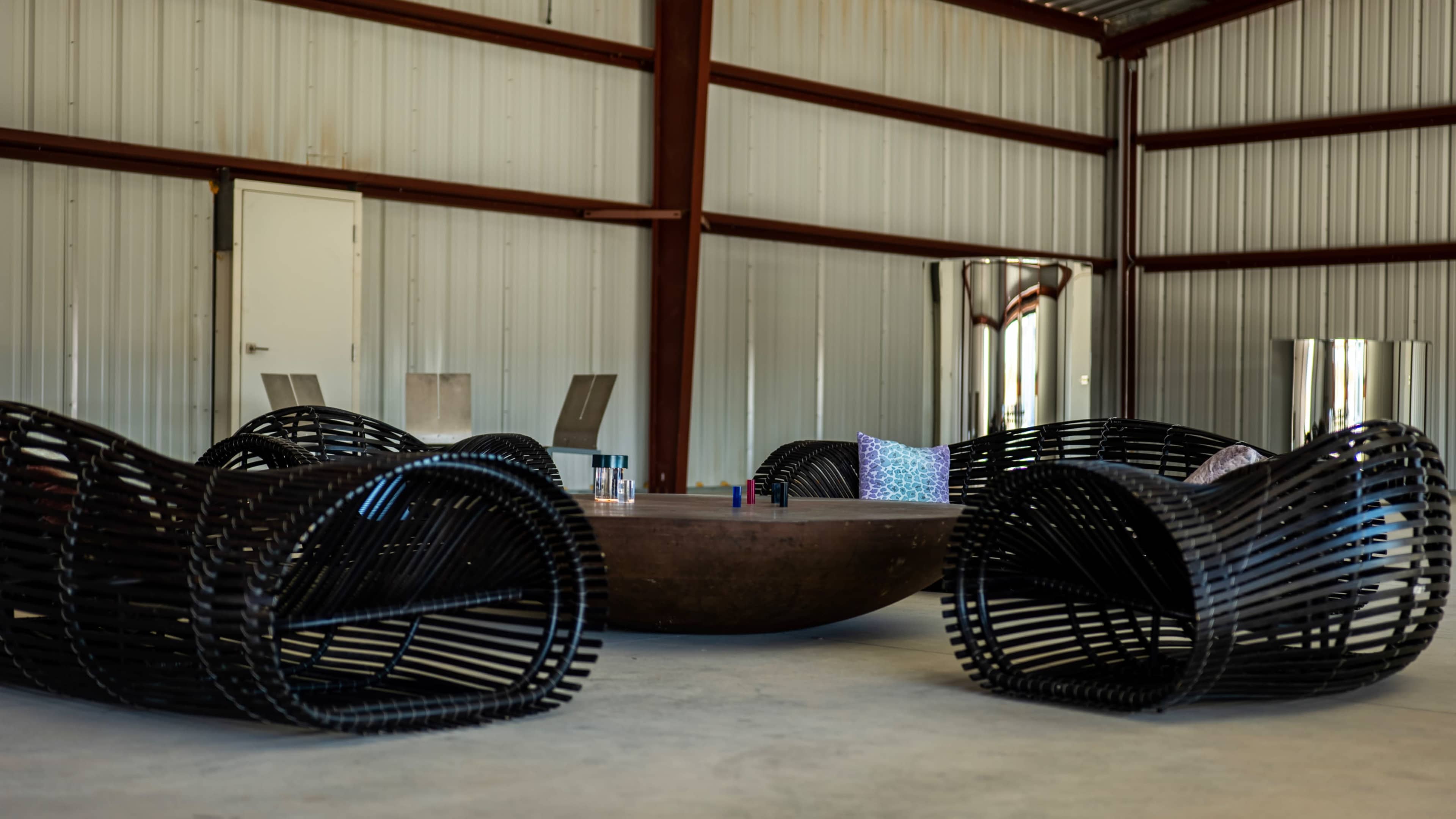 A modern seating area features two curved black chairs and a round wooden table in an industrial-style space with metal walls.