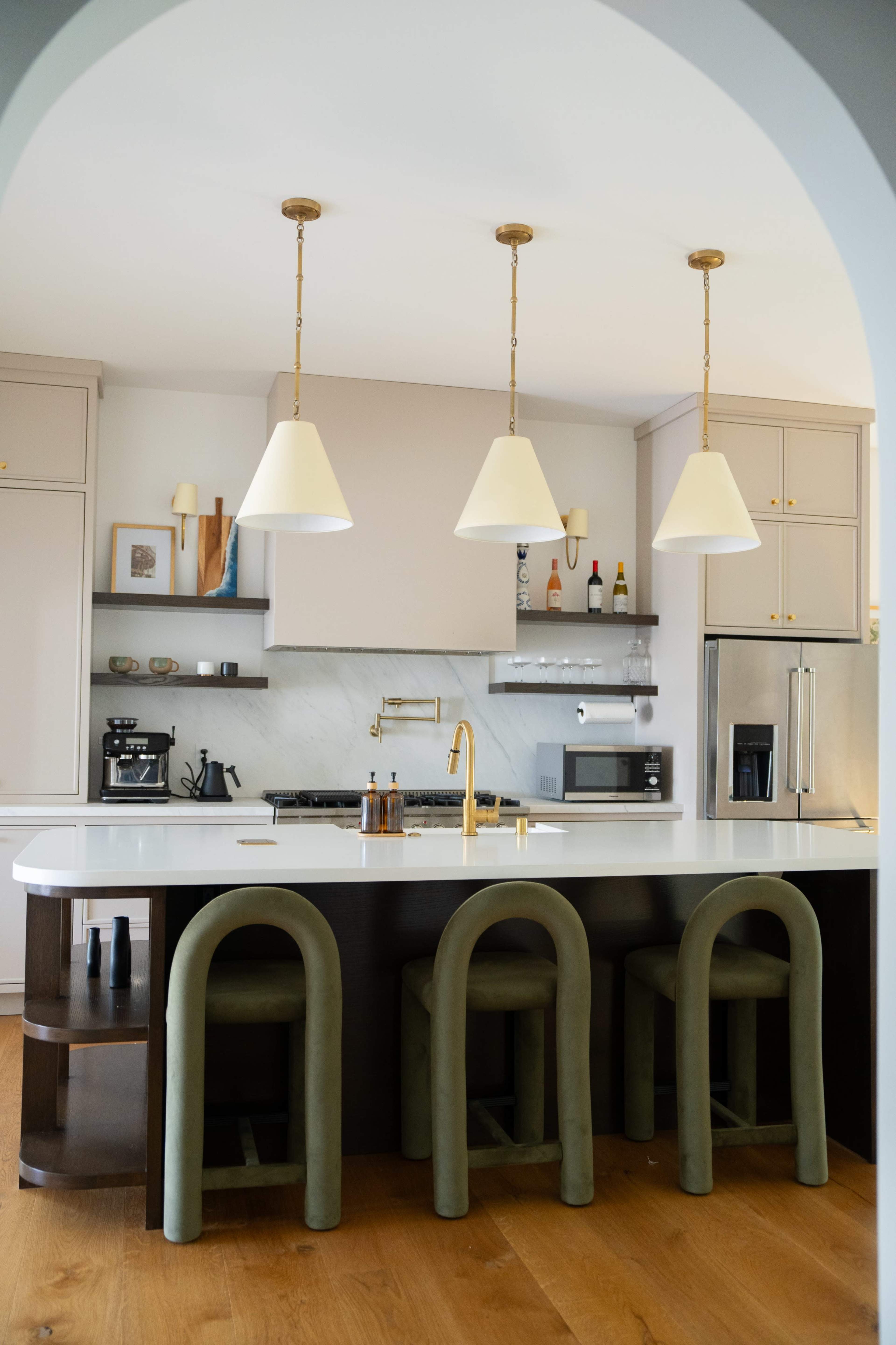 A modern kitchen features a large island with three green stools, pendant lighting, and stainless steel appliances.