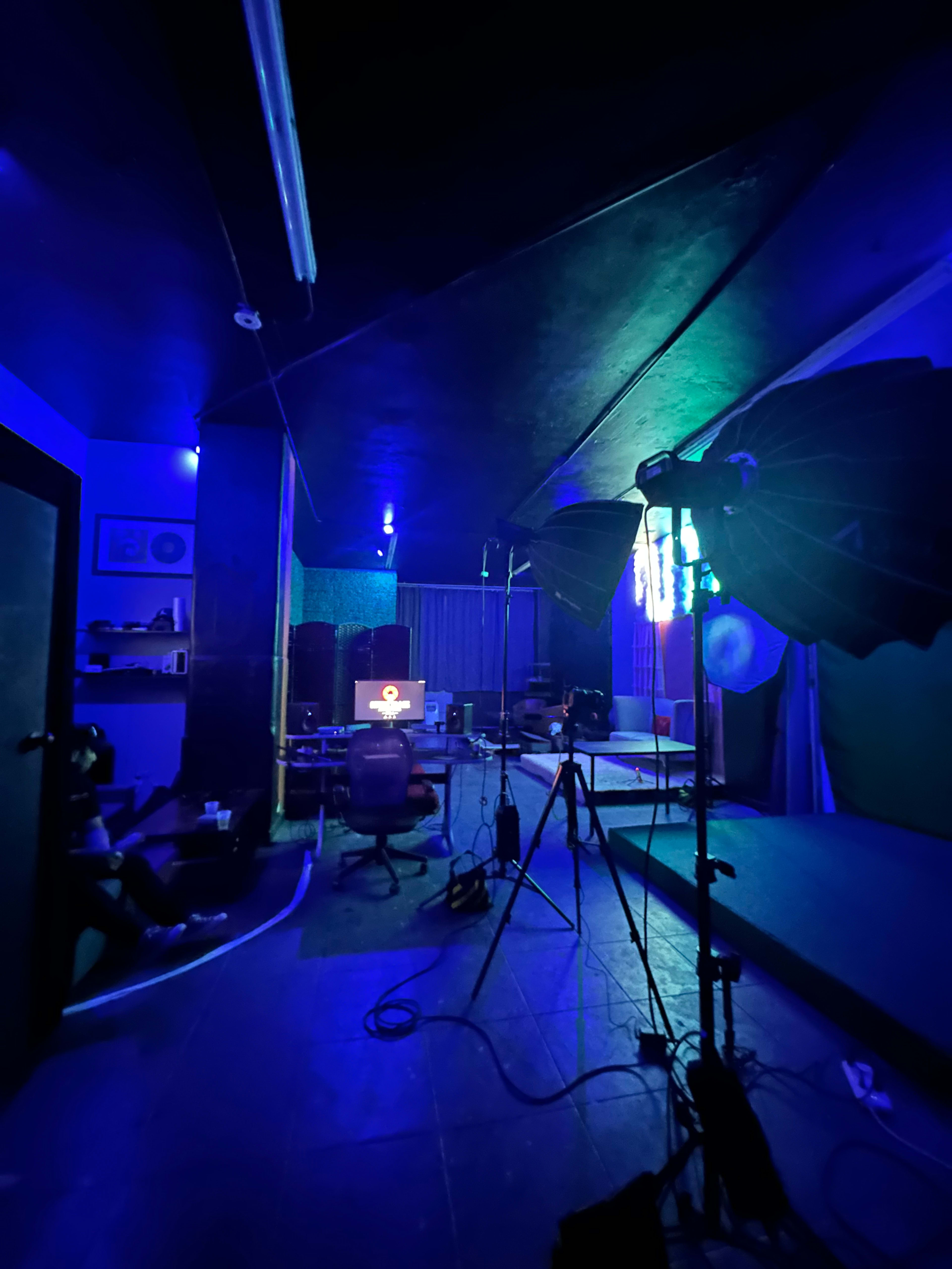 A dimly lit studio space with blue lighting, equipped with photography studio lights and a chair in front of a computer setup.