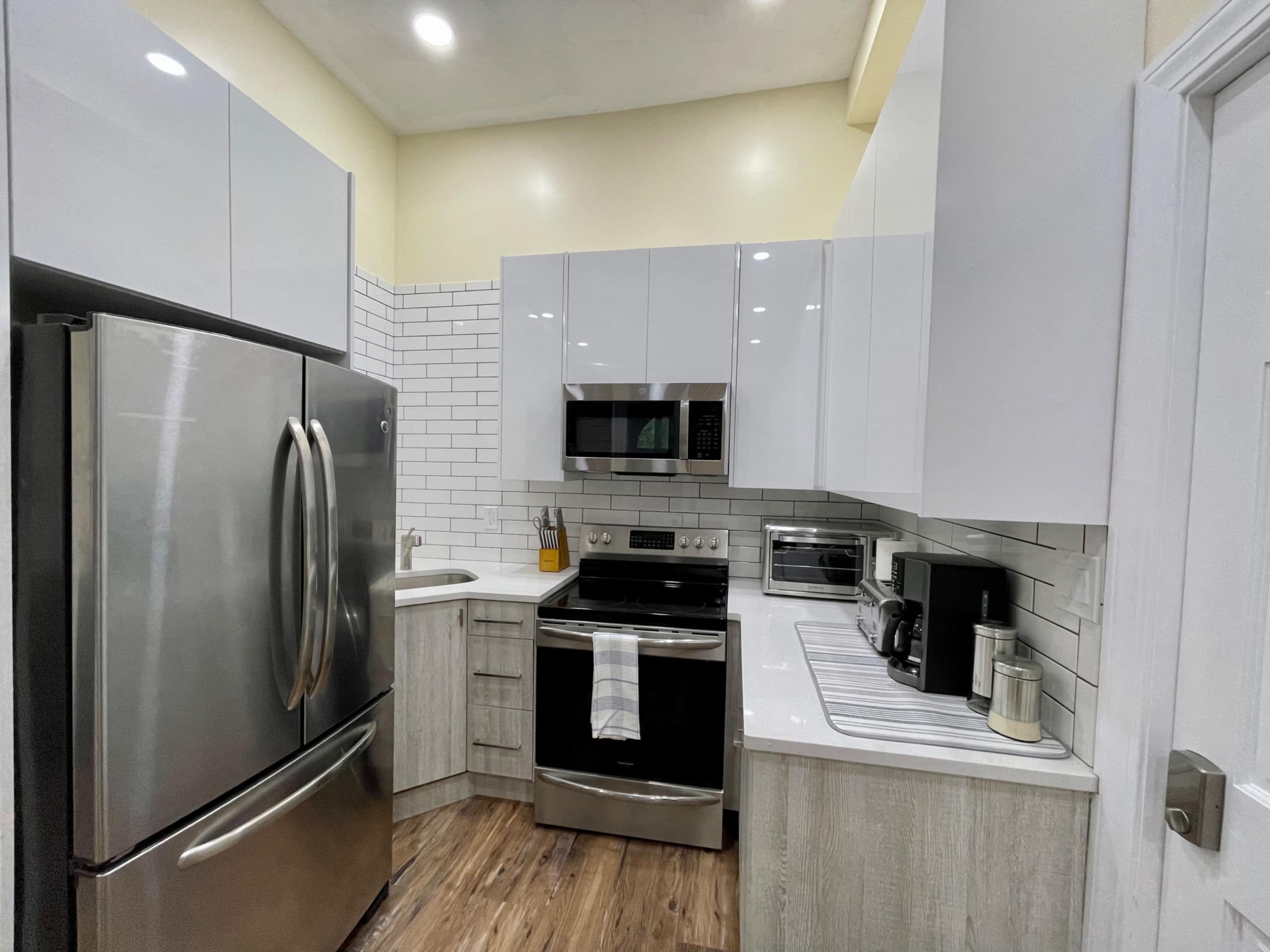 A modern kitchen with stainless steel appliances, white cabinetry, and a combination of tiled and wooden flooring.