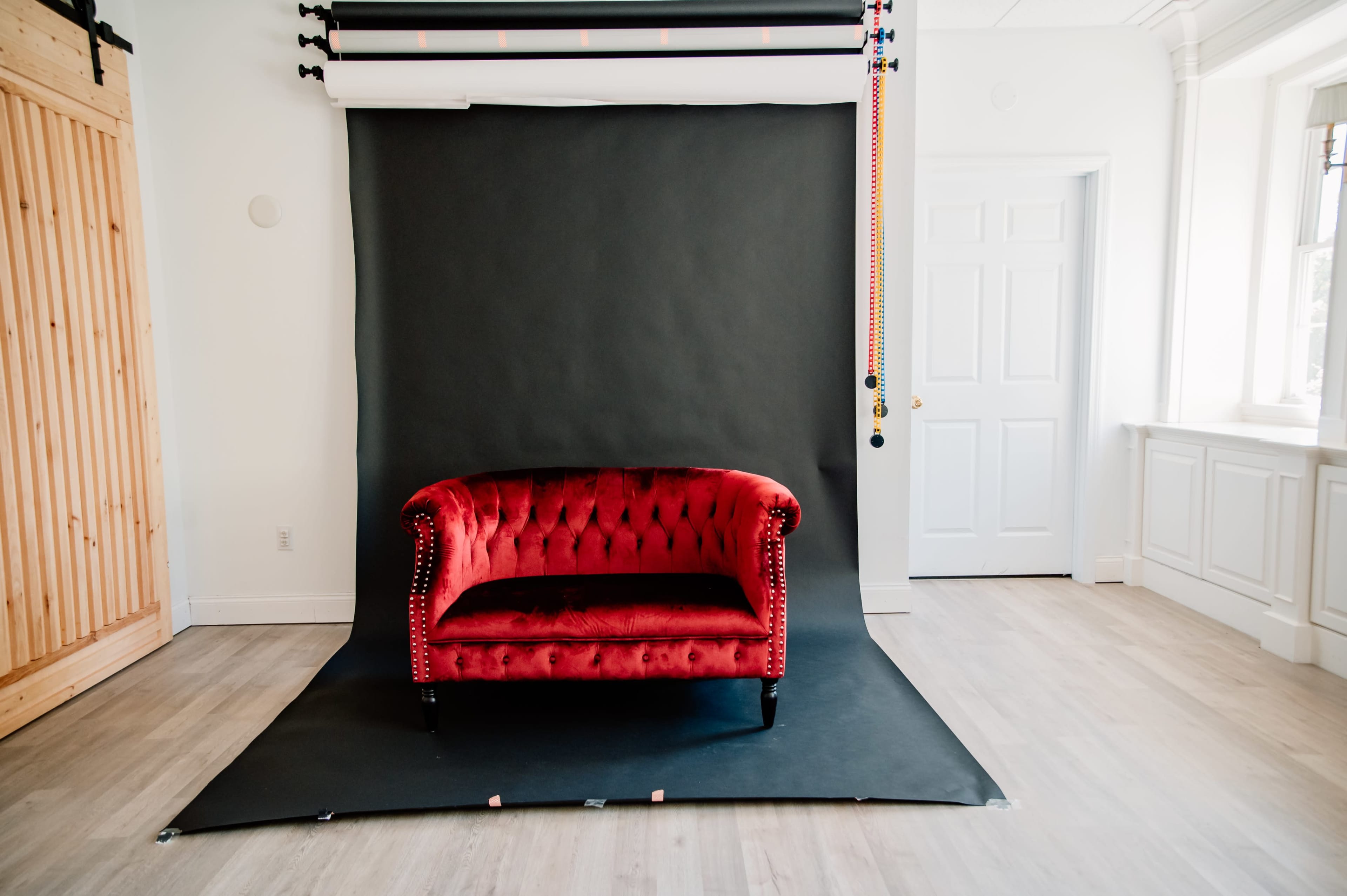 A red tufted sofa is positioned in front of a dark backdrop in a spacious, well-lit room.