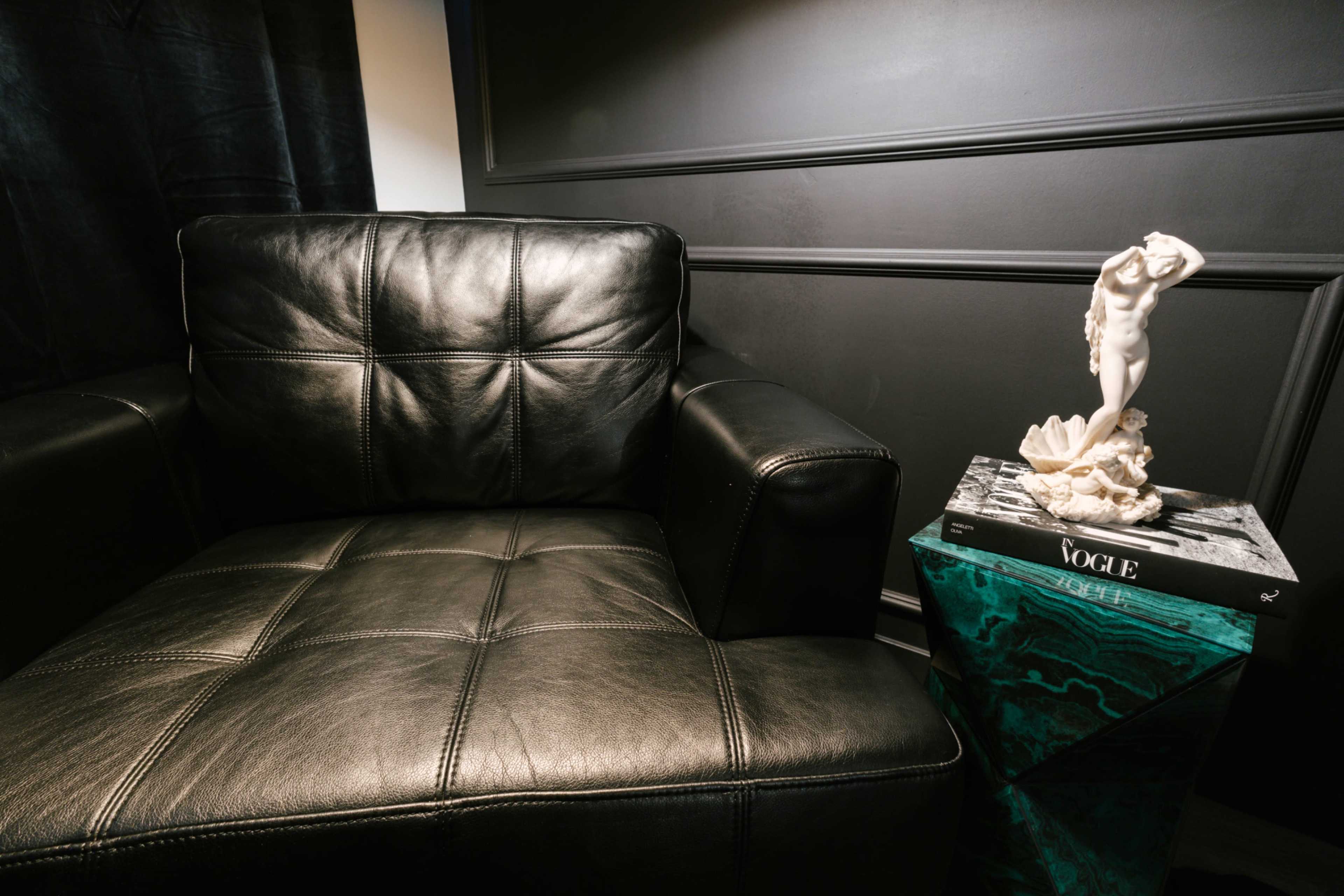The image shows a black leather armchair next to a decorative table displaying a figurine and a magazine.