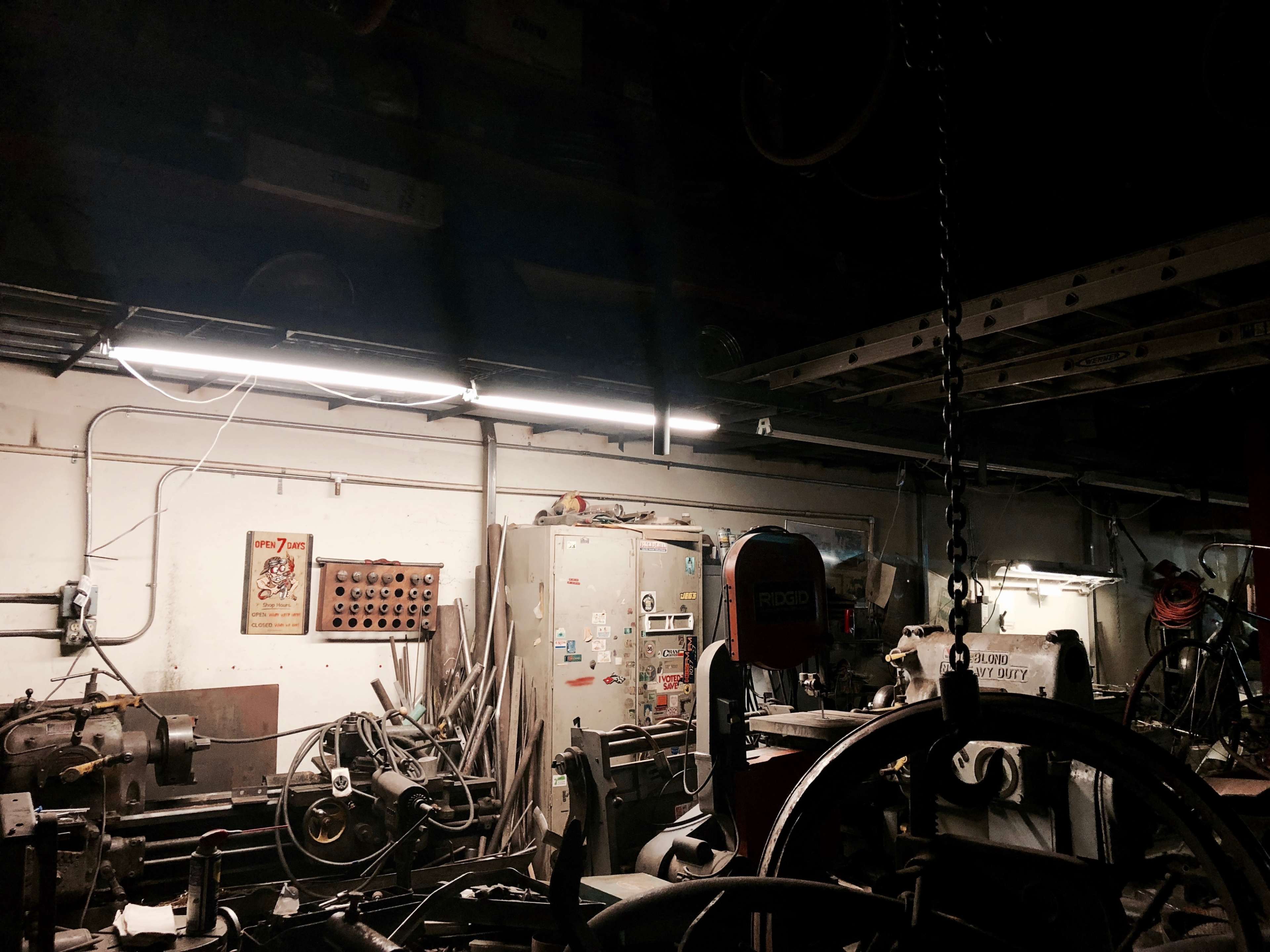 A dimly lit workshop with various tools and machinery scattered around, a storage cabinet, and a poster on the wall.