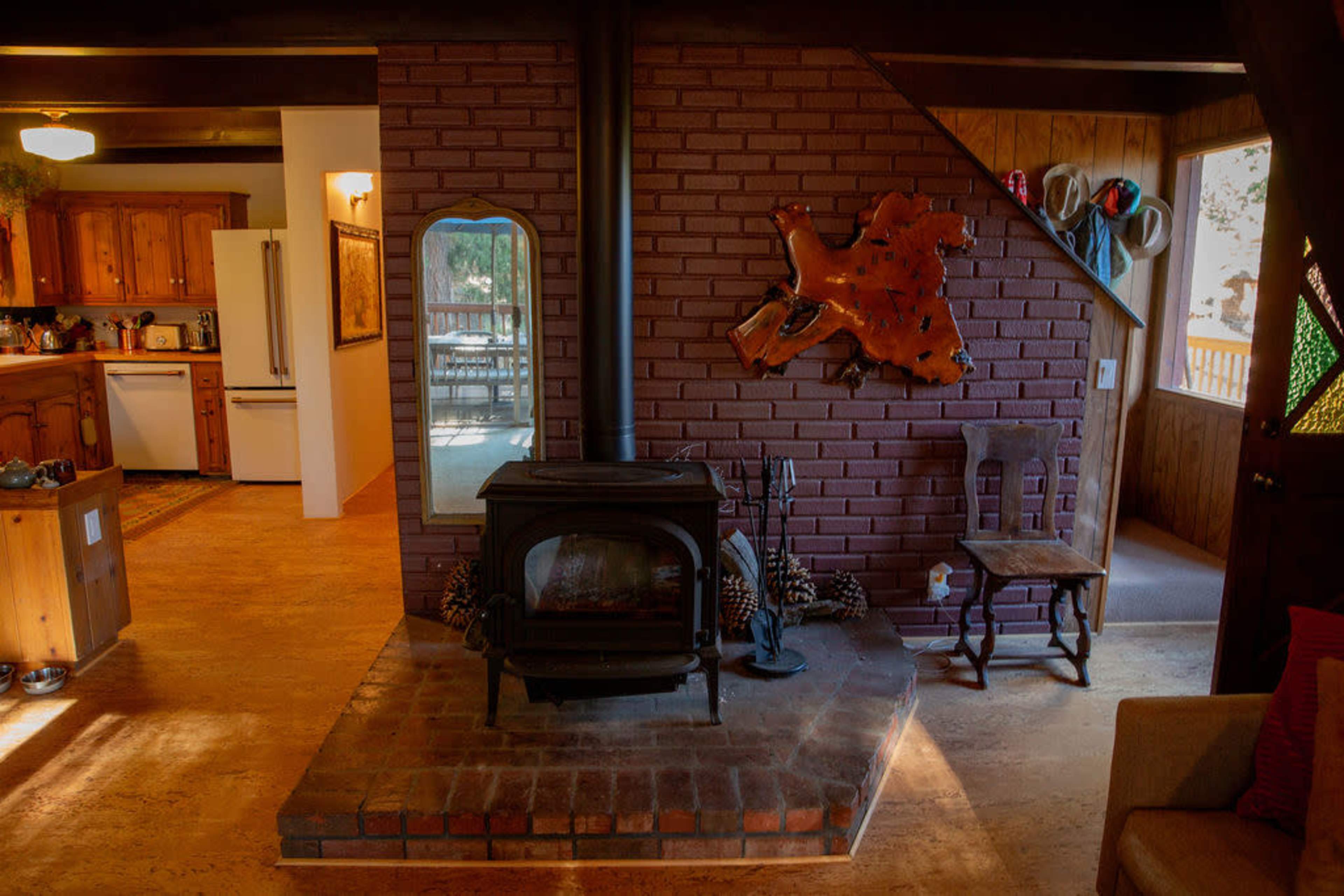 A cozy interior with a wood stove on a brick platform, adjacent to a kitchen and dining area, and decorated with a wooden wall hanging.