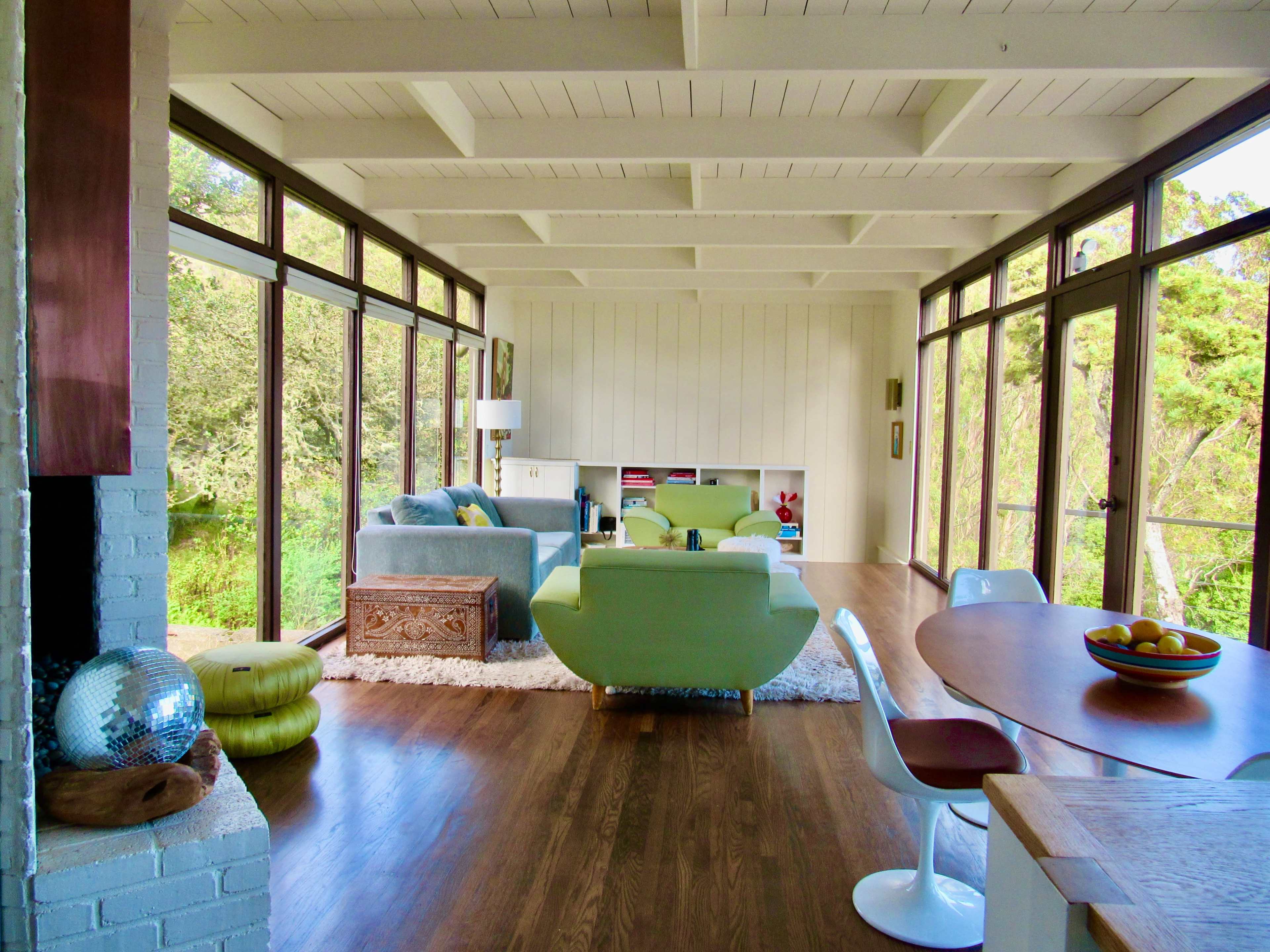 A modern living space with large windows, hardwood flooring, green furniture, and a dining area featuring a round table.