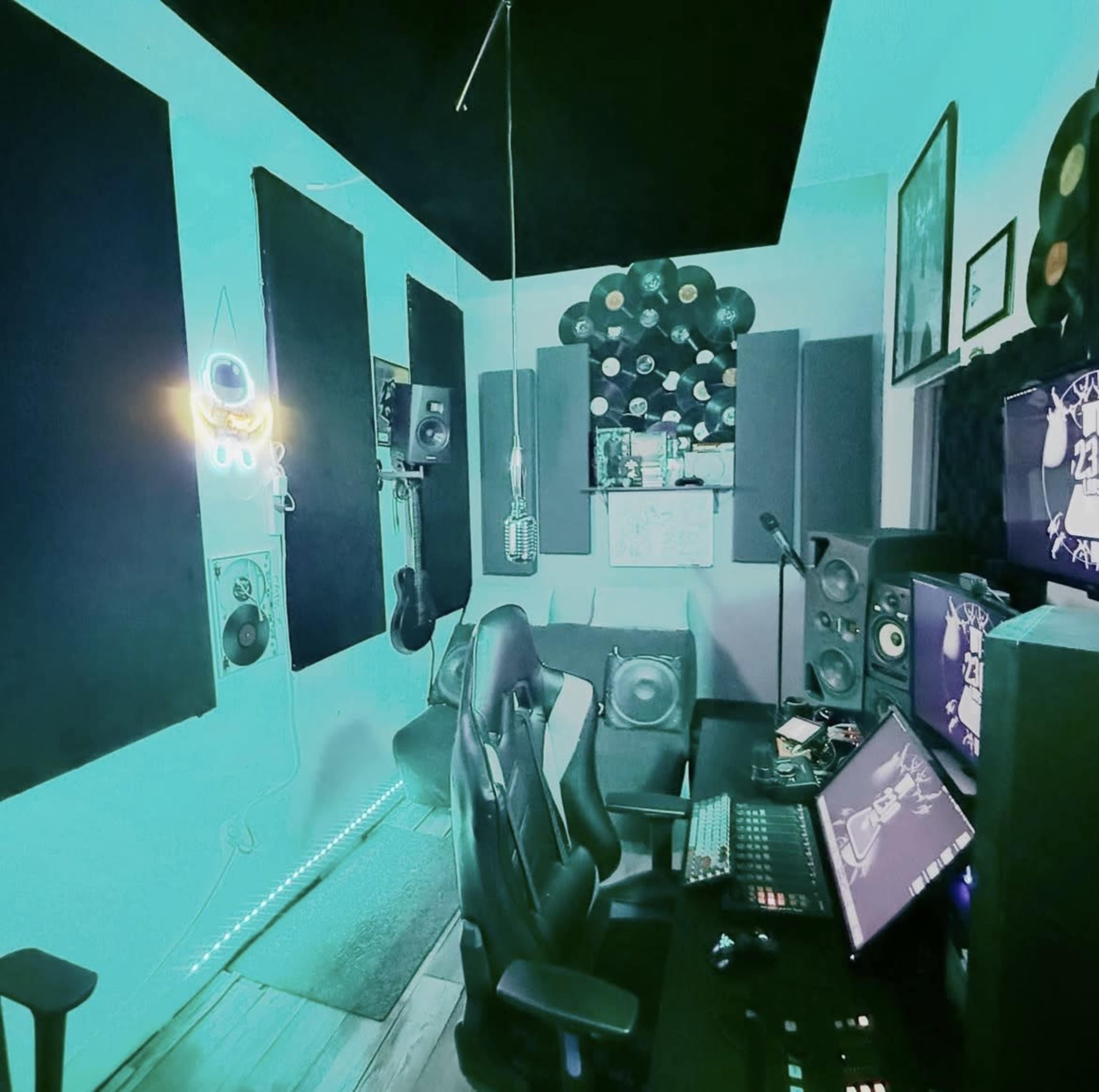 The image shows a music recording studio with soundproofing panels, a desk setup with digital equipment, and ambient lighting.