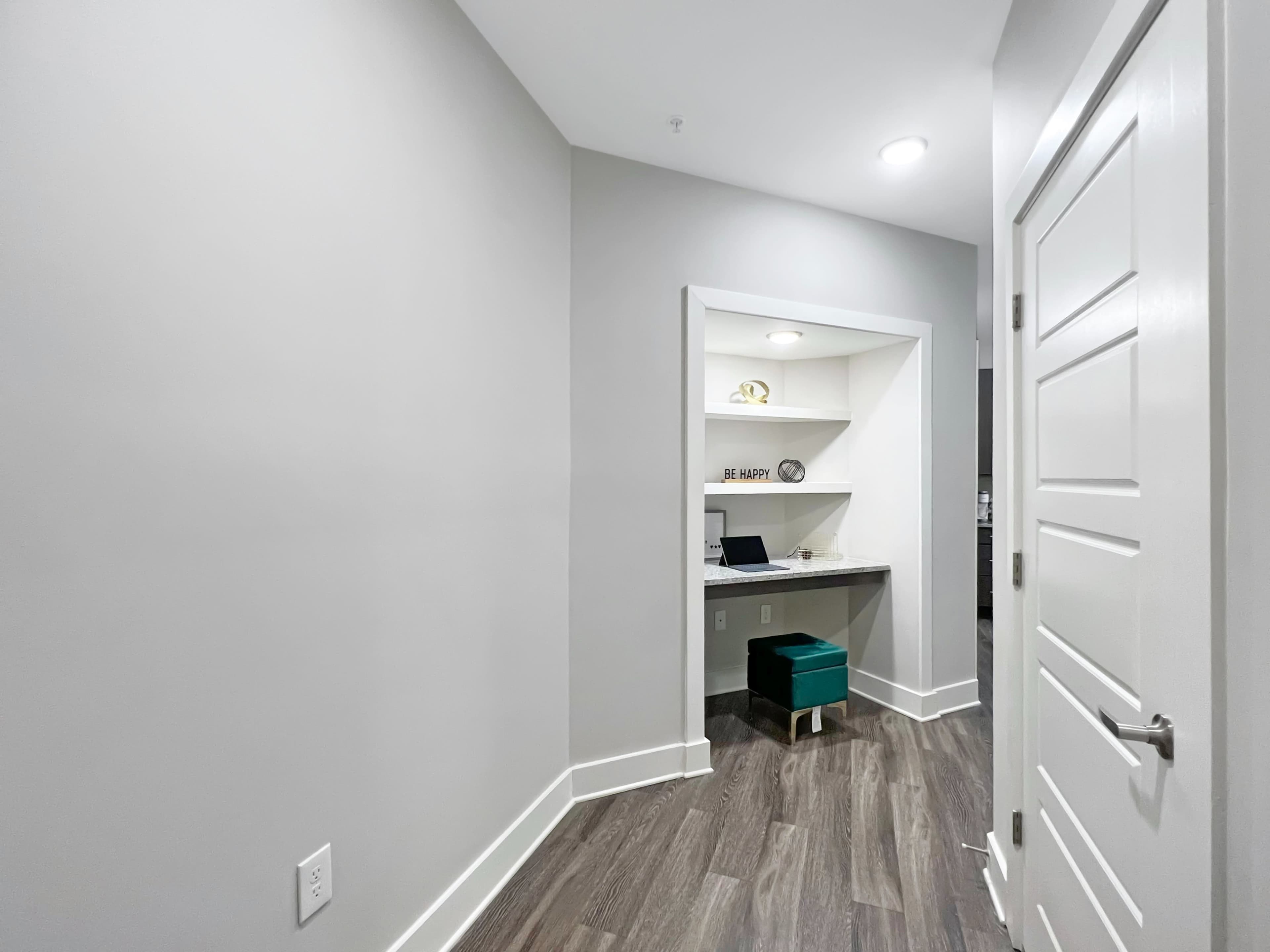 A small hallway leading to a nook with a desk and shelves, featuring a laptop and a decorative sign.