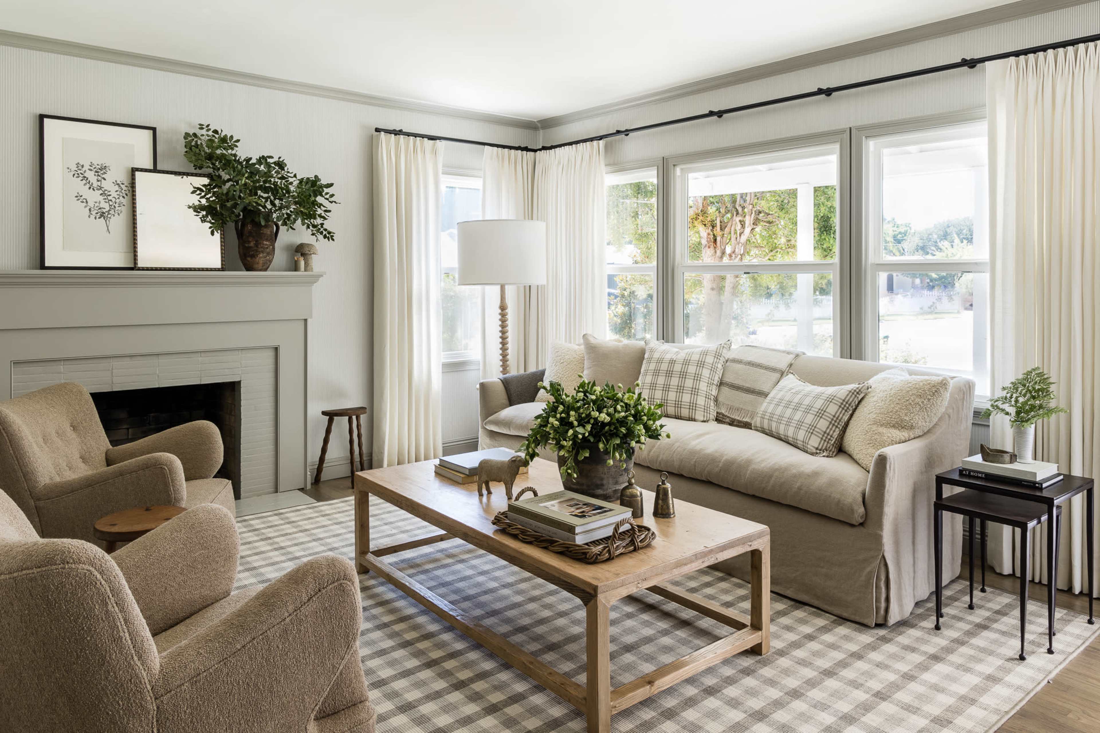 A cozy living room with a sofa, two armchairs, a coffee table, and large windows dressed with light curtains.