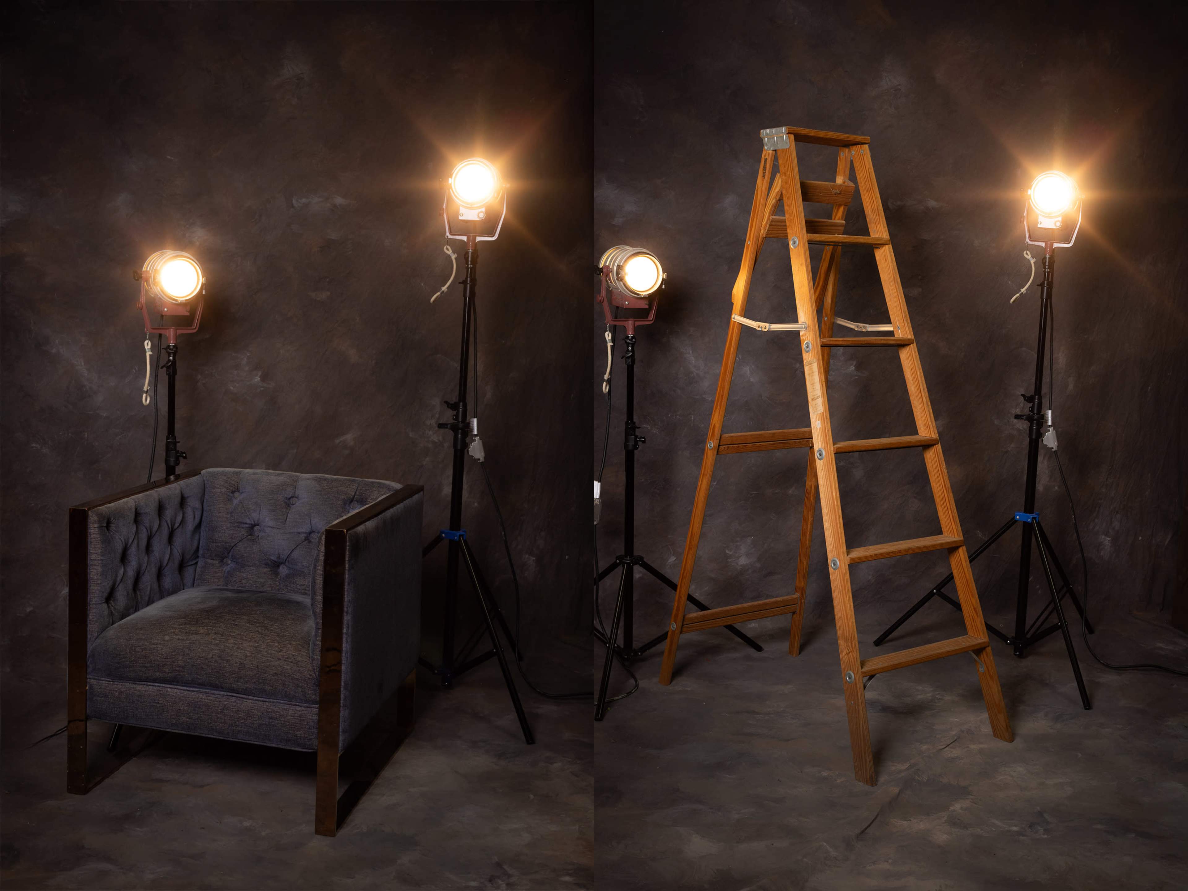 The image displays a tufted armchair on the left and a wooden ladder on the right, both positioned under bright stage lights against a dark backdrop.