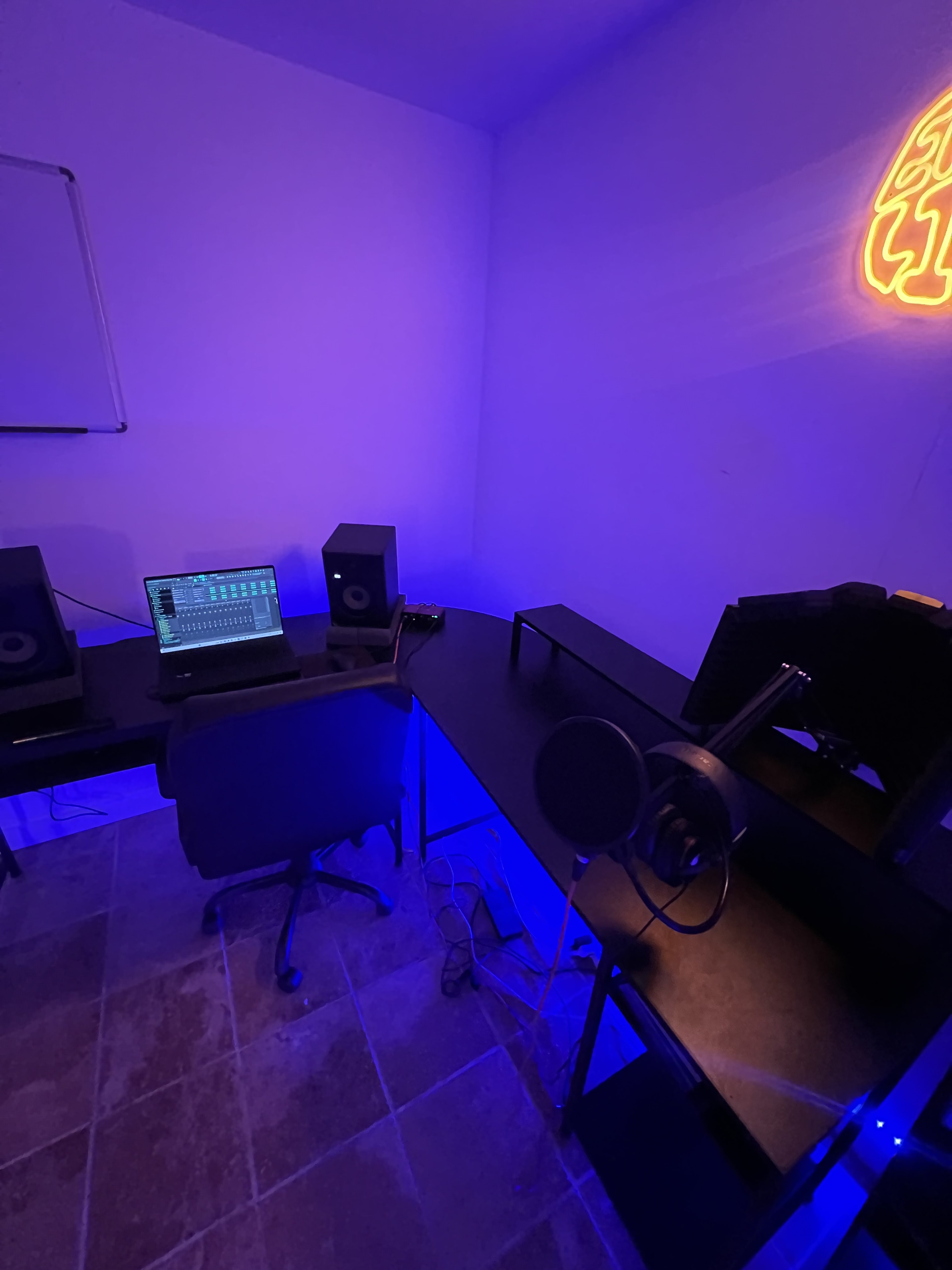 A music production studio features a laptop, audio monitors, and a microphone in a room illuminated with blue lighting.