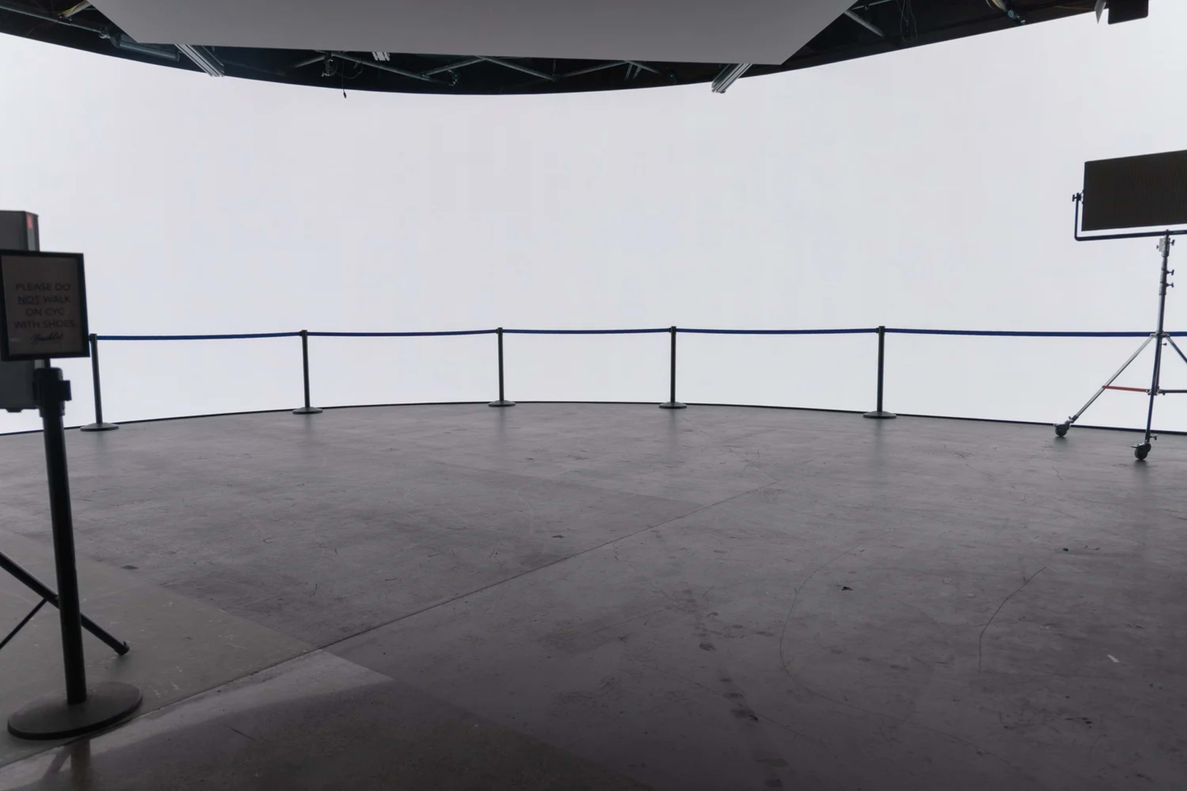 The image shows a circular studio space with a clean, white backdrop and a barrier rope surrounding the area.